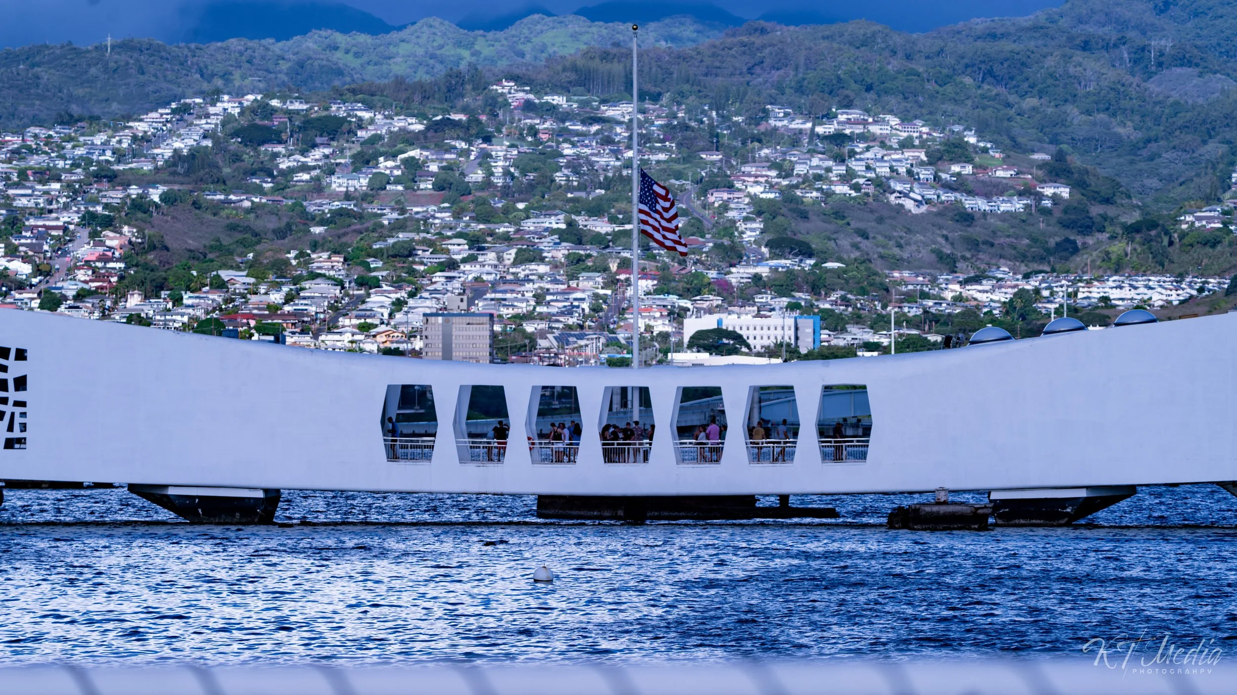 The San Francisco Museum of Modern Art's boat on the water with a view of a cityscape and green hills in the background, American flag flying on the boat.