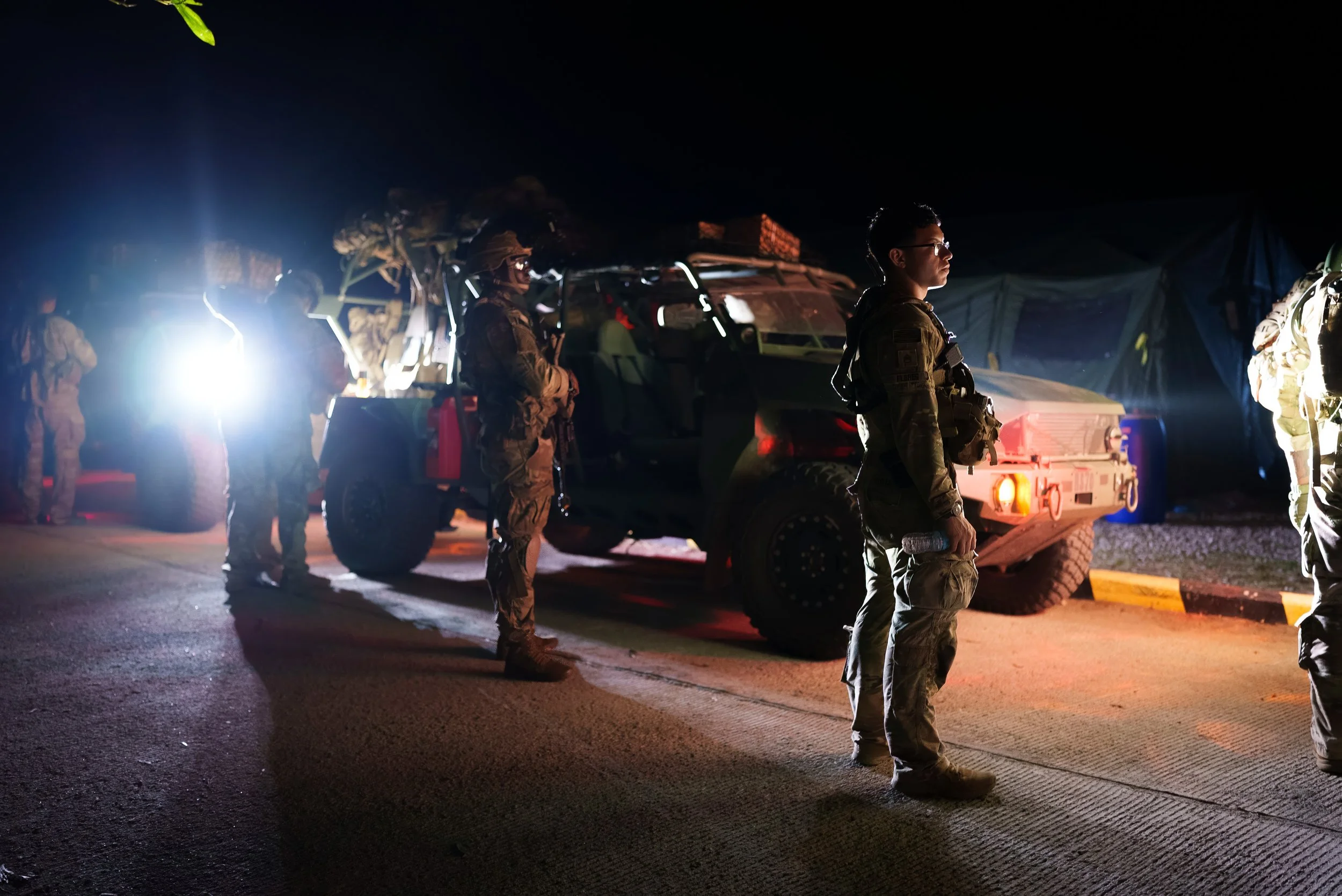 Military personnel standing near military vehicles at night.