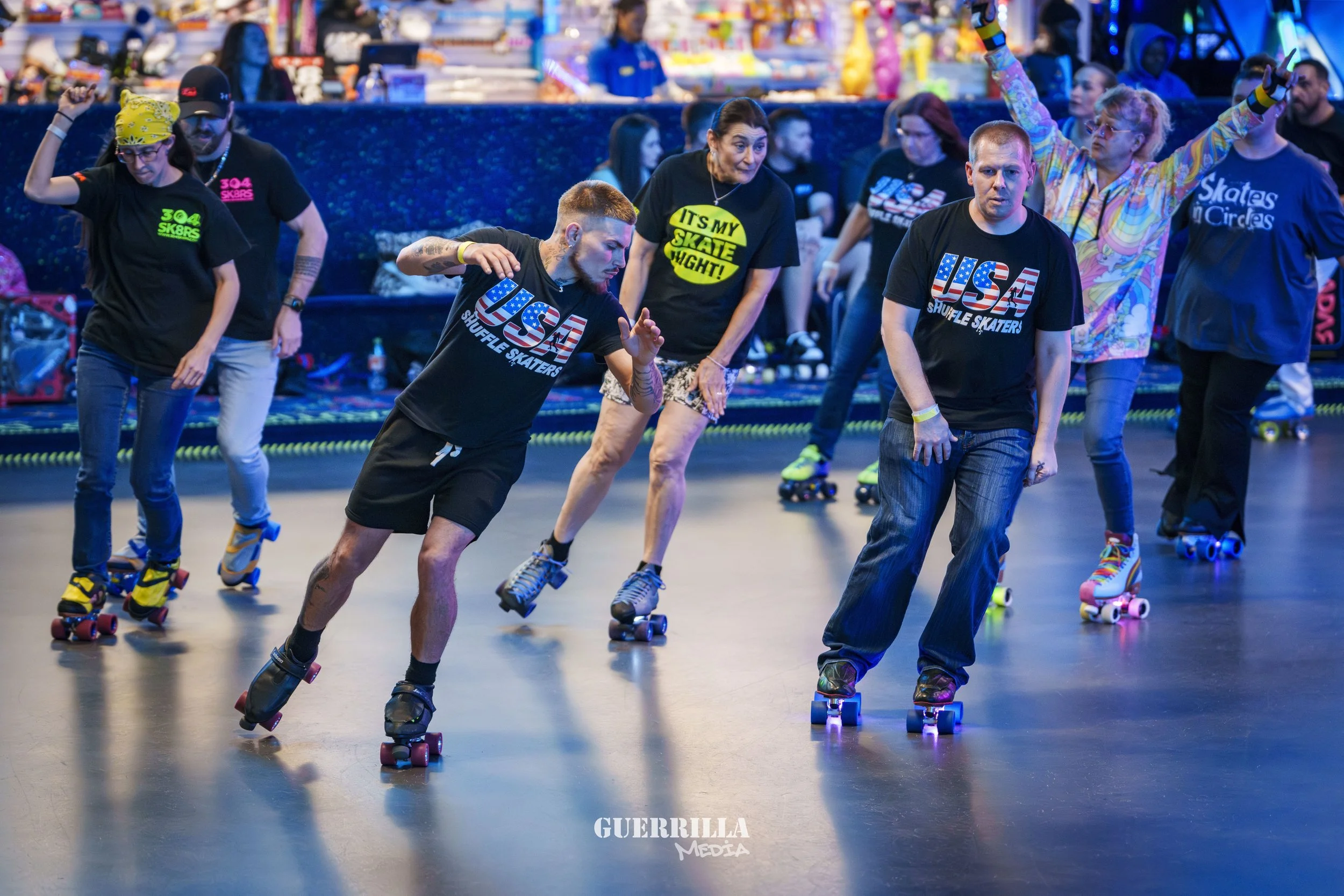 People roller skating at an indoor rink, wearing casual clothes, some with themed t-shirts, and enjoying the activity.