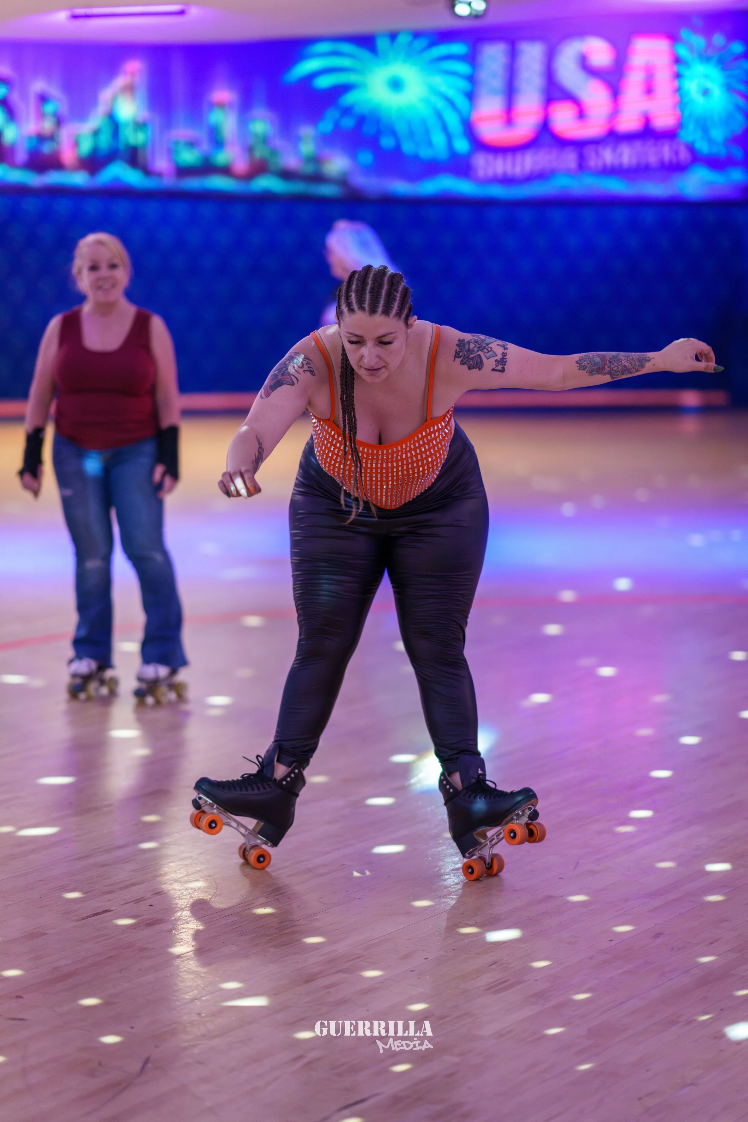 A woman roller skating indoors with a woman in the background, neon USA sign, and colorful fireworks display on the wall.