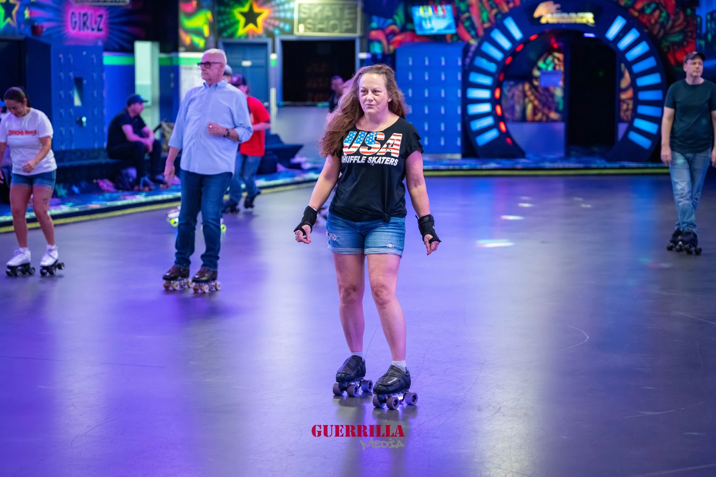A woman roller skating at an indoor roller rink with colorful neon lights and other skaters in the background.