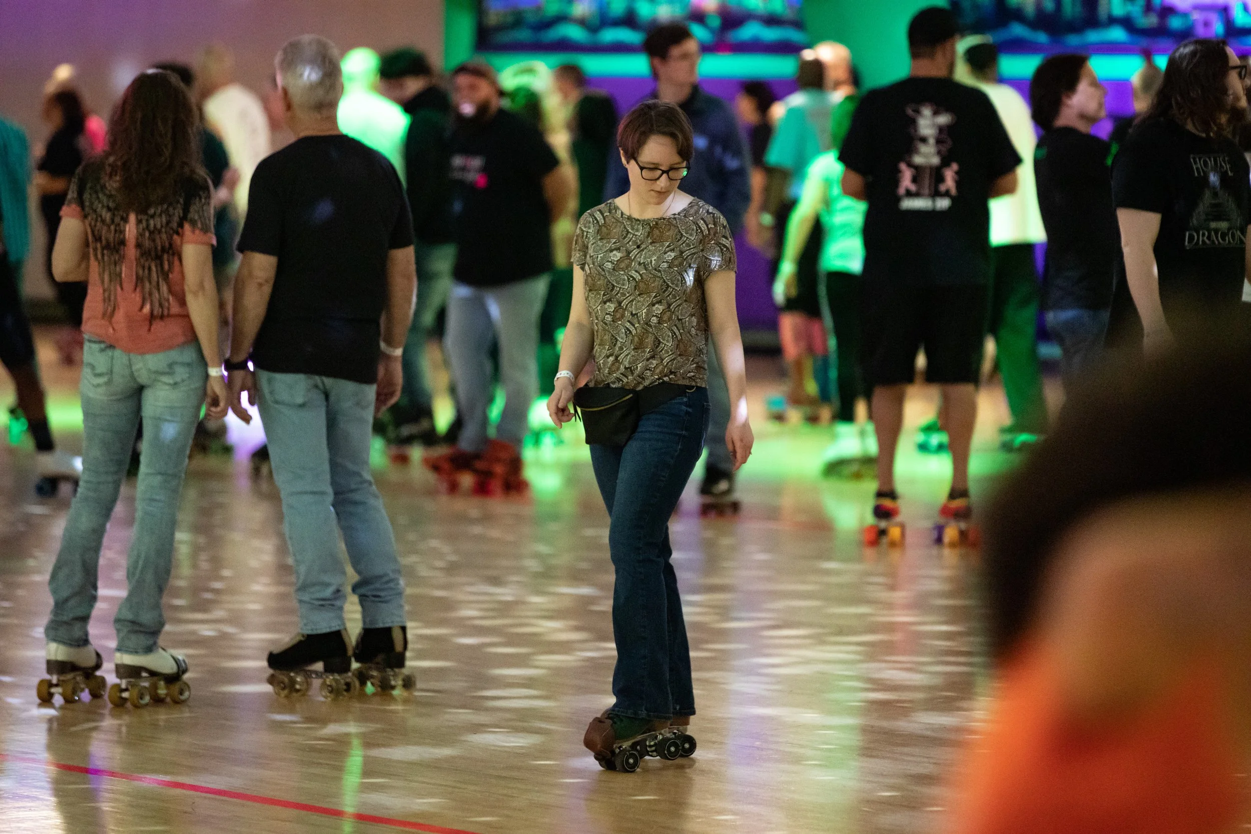 People roller skating on an indoor rink with a colorful, neon-lit background.