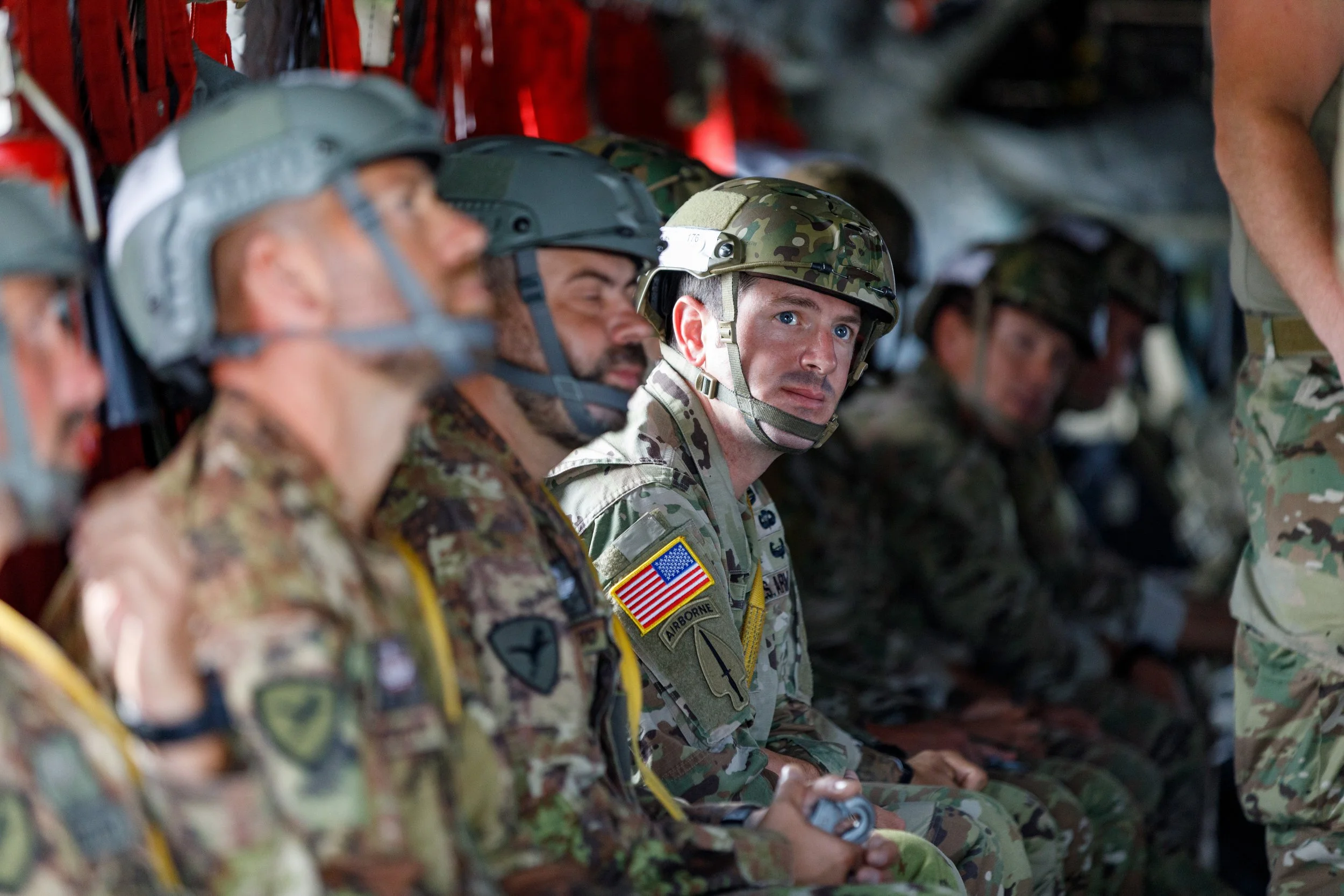 U.S. soldiers seated inside a military aircraft, wearing camouflage uniforms and helmets, preparing for deployment or mission.