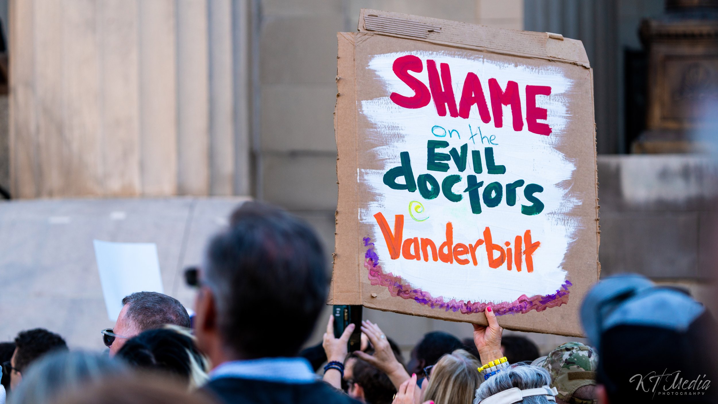 A protest crowd holding a handmade sign that reads 'Shame on the evil doctors @ Vanderbilt.'