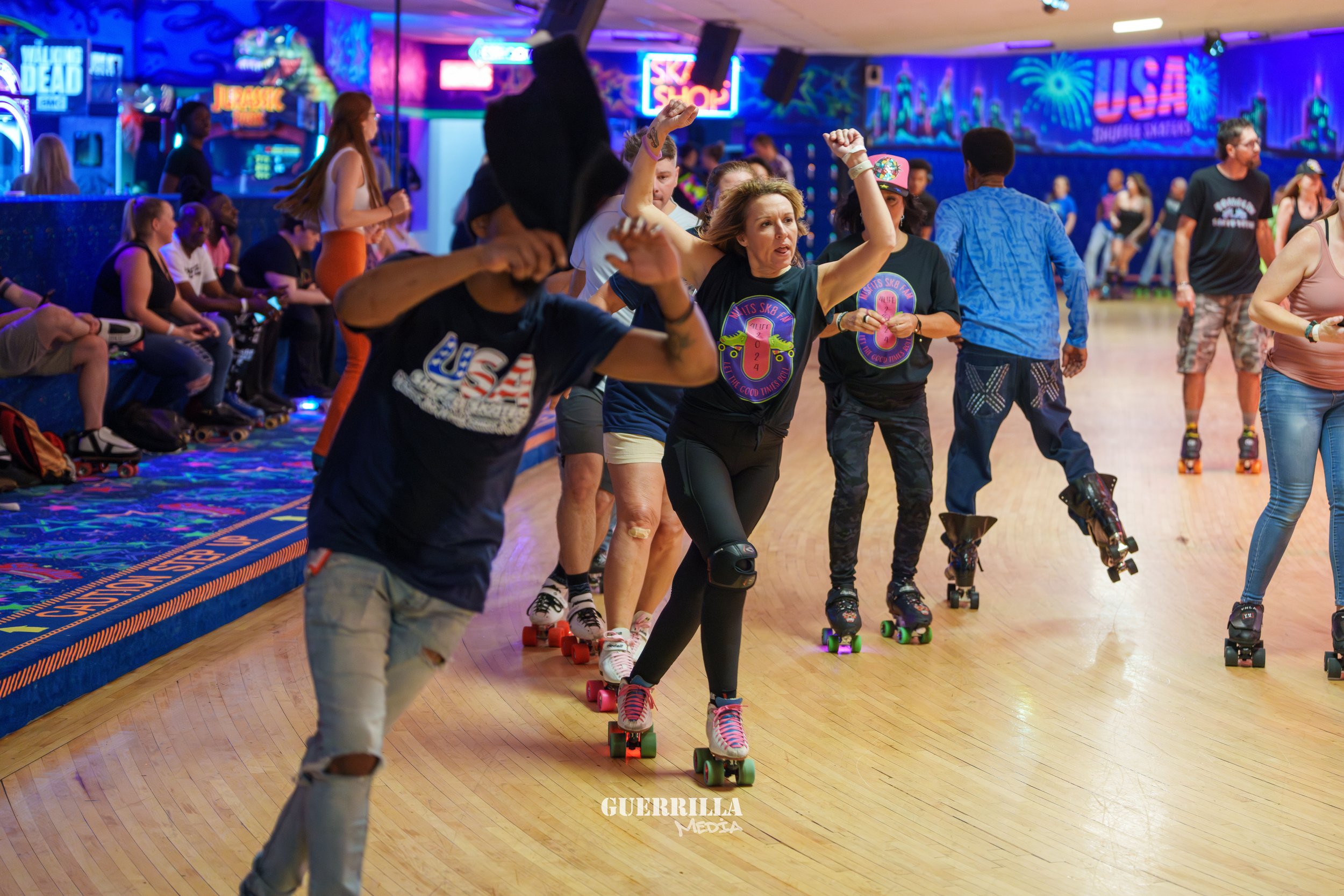 People roller skating at an indoor skate rink with vibrant, colorful neon lights and walls decorated with US and country-themed graphics.