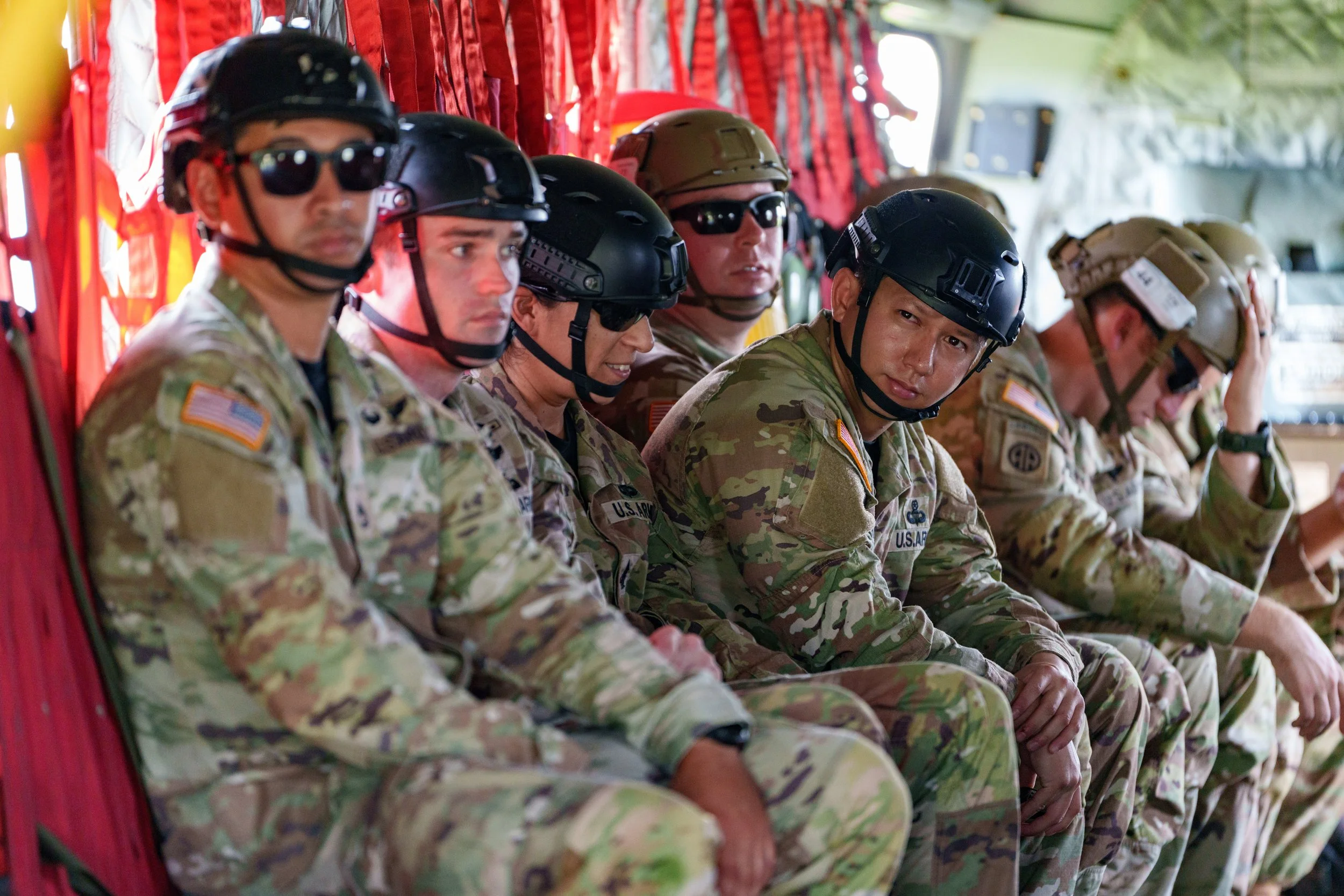 A group of soldiers in camouflage uniforms and helmets sitting inside a military aircraft.