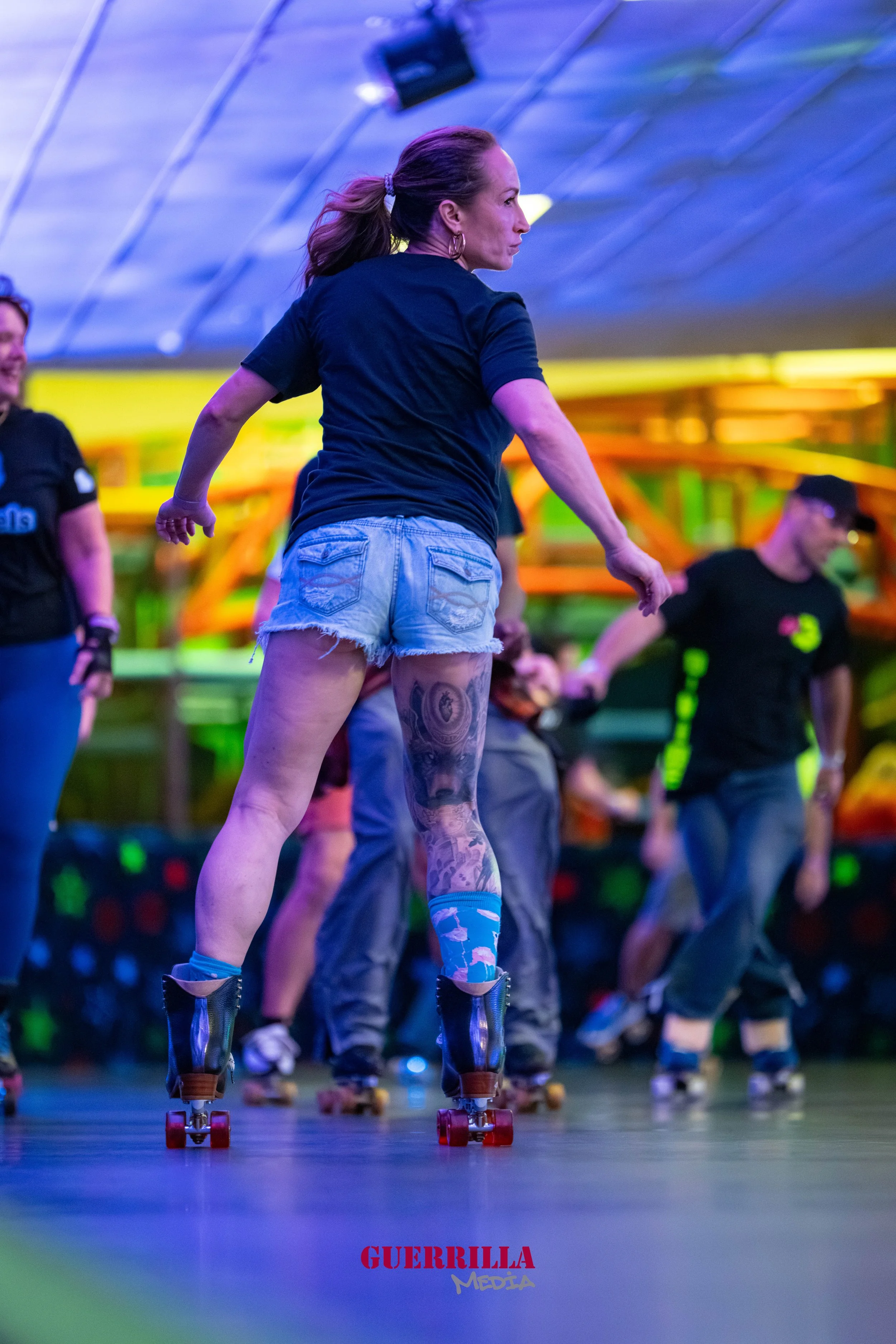 A woman roller skating indoors on a roller rink with colorful, neon lighting, surrounded by others roller skating.