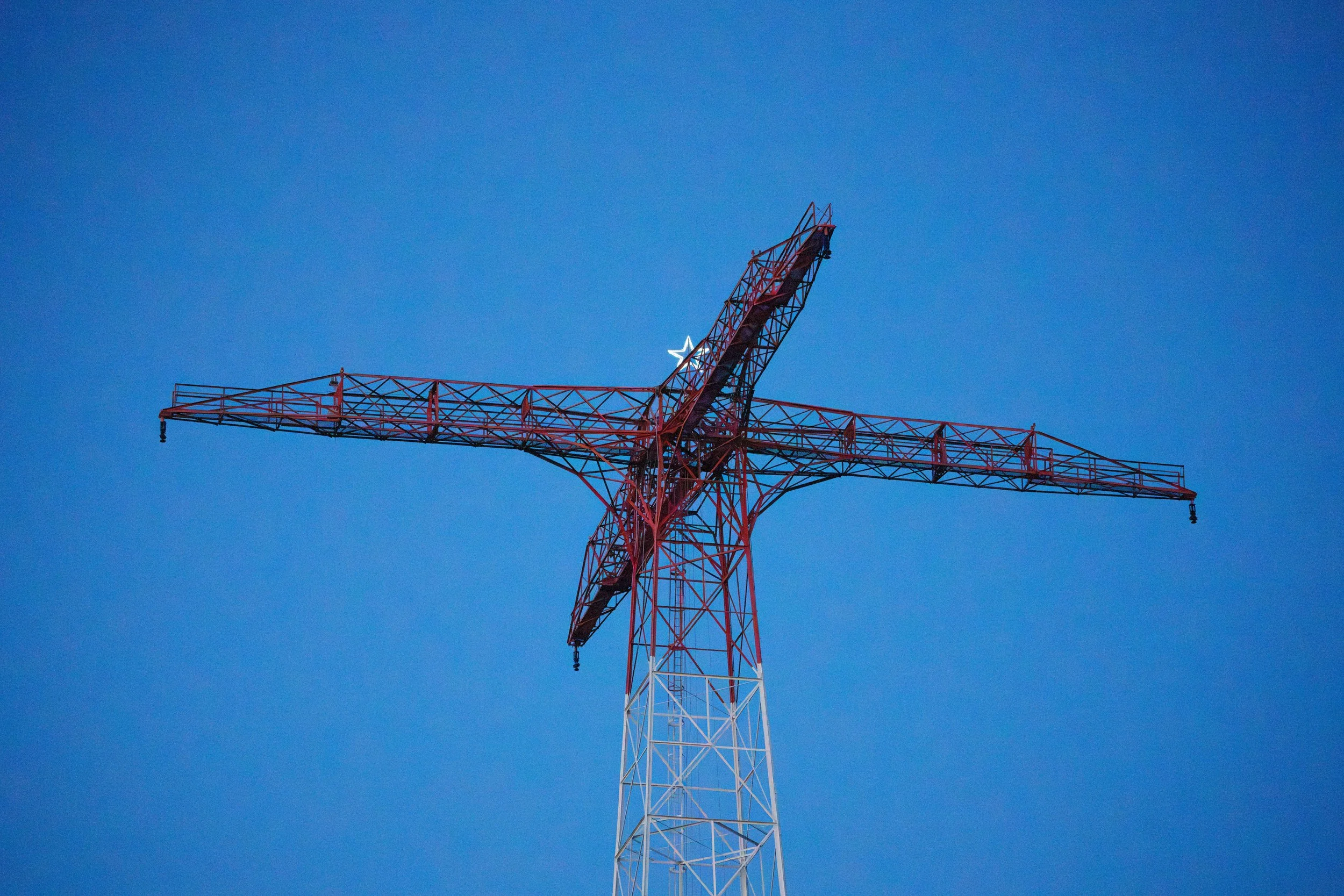 Looking up at a tall red and white construction crane against a clear blue sky.