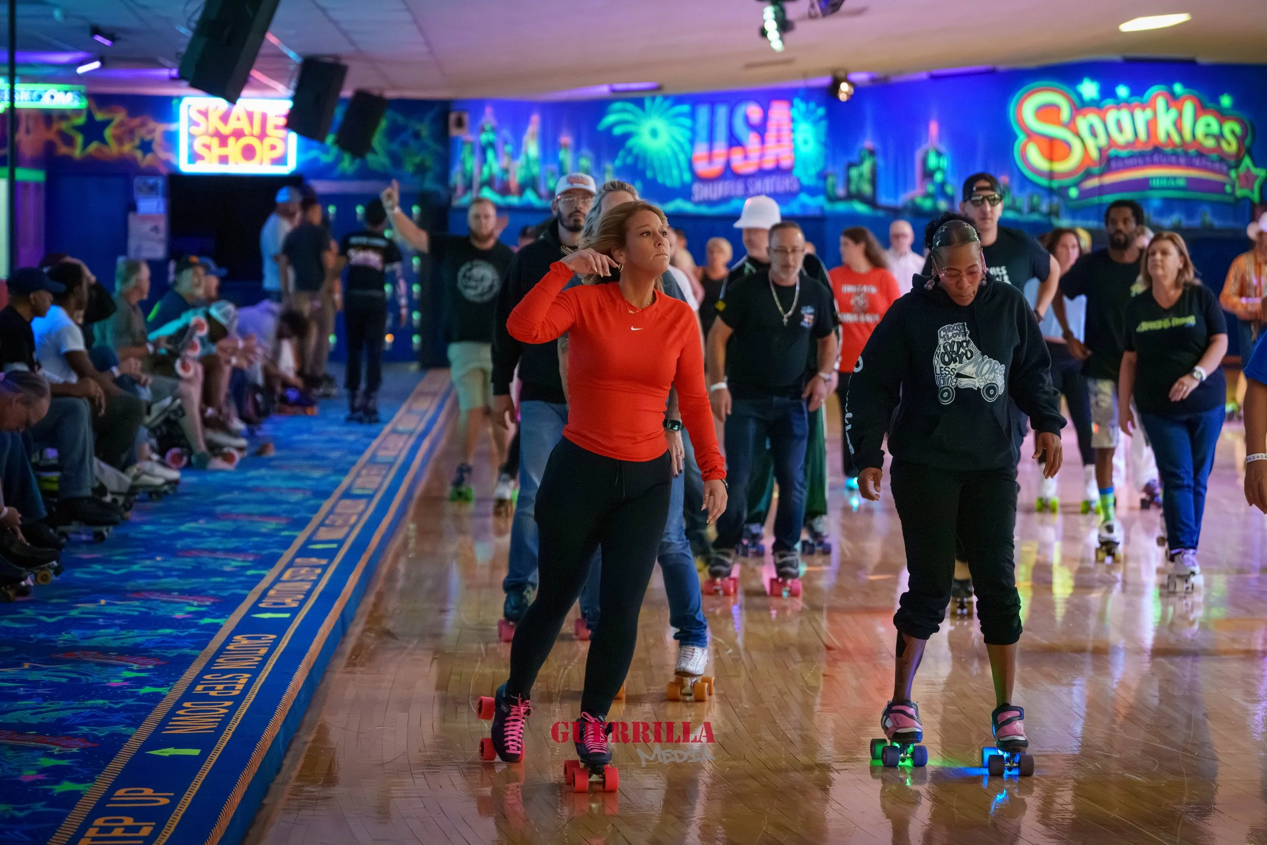 People roller skating indoors at an amusement center with colorful neon signs and a decorated wall backdrop.
