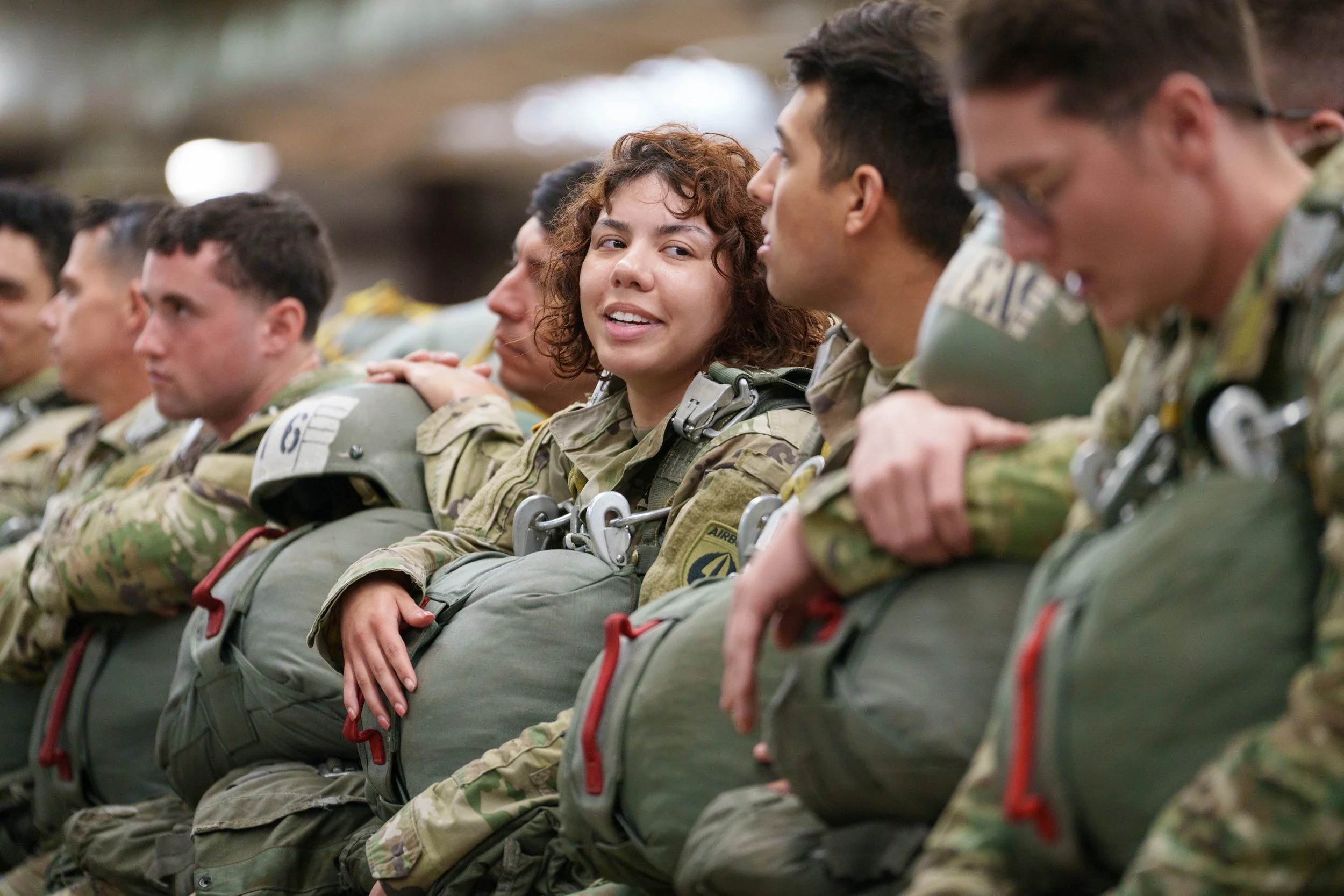 Group of soldiers in military uniform sitting in a row, with one female soldier talking.