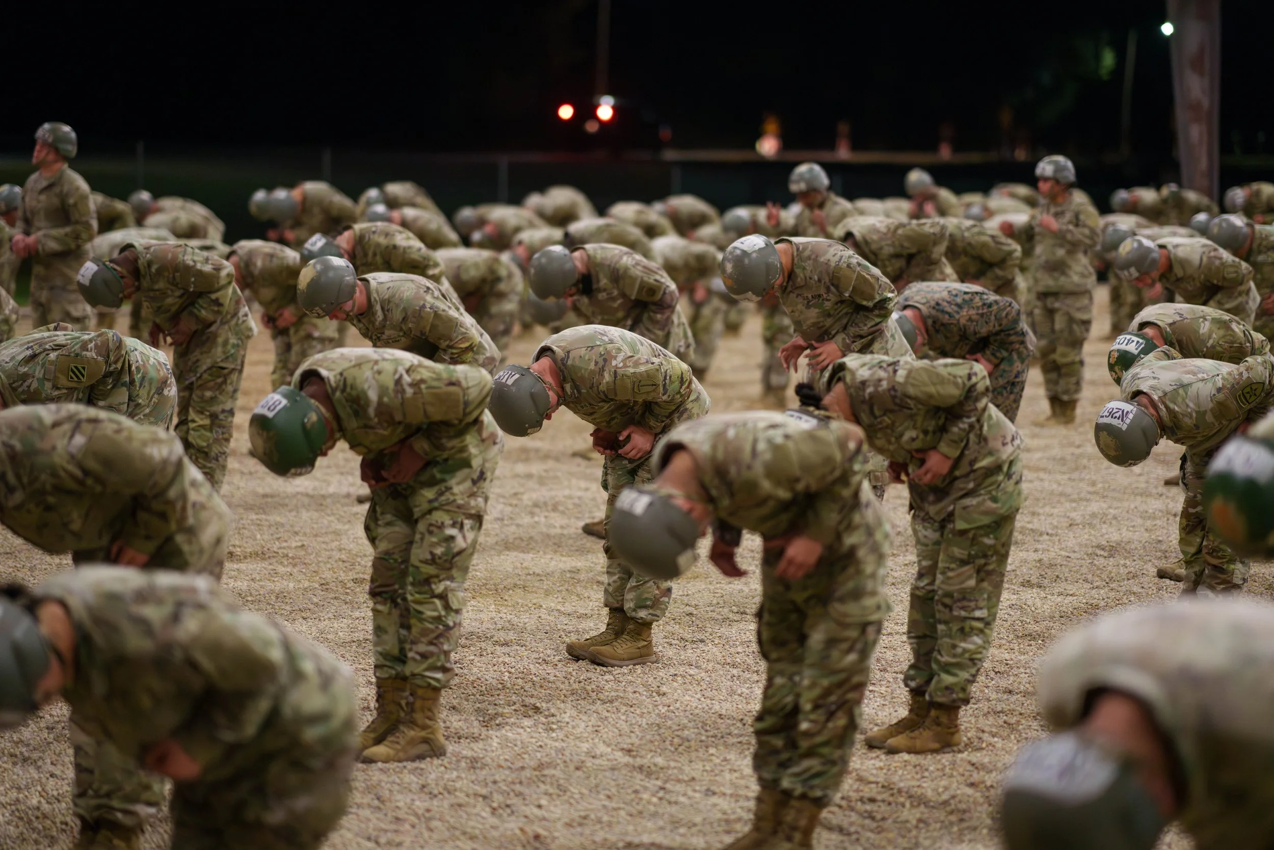 Military personnel in camouflage uniforms and helmets practicing a drill outdoors at night.