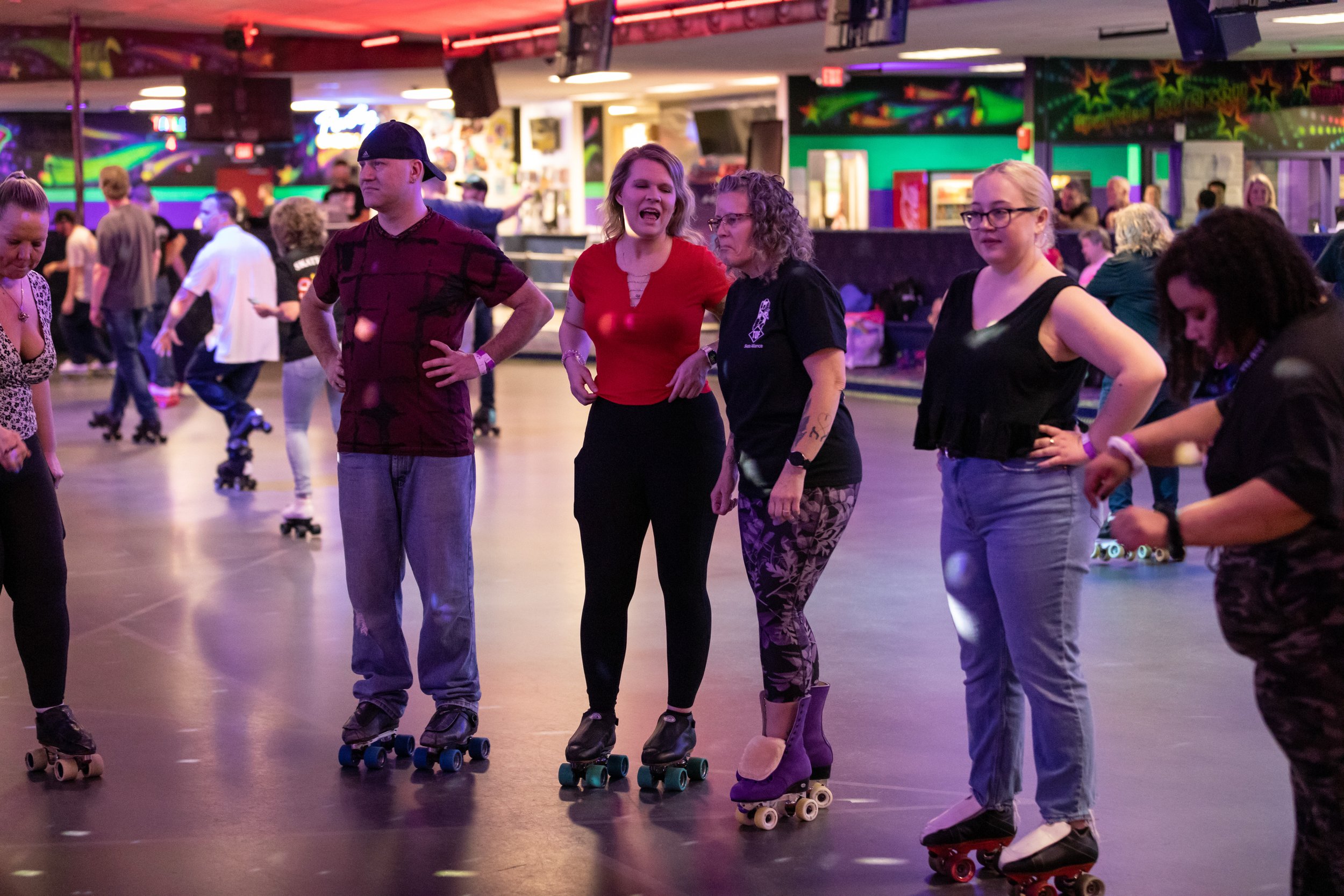 People roller skating at an indoor roller rink with colorful lights and graffiti-like wall art in the background.