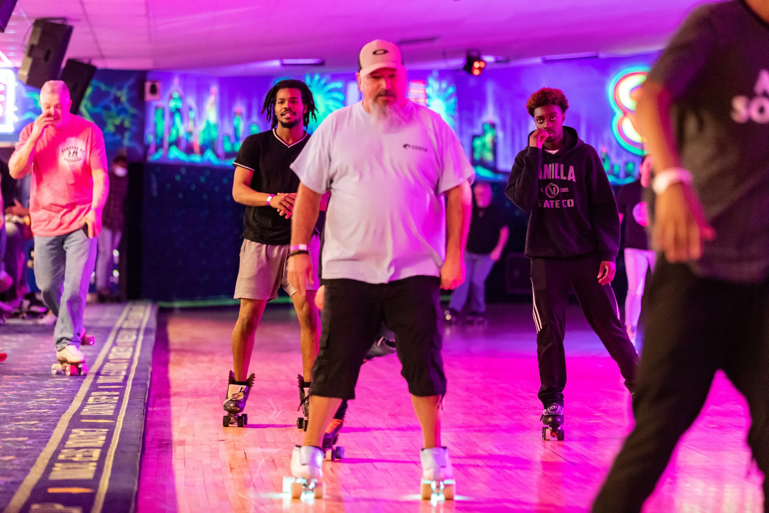 People roller skating in a neon-lit roller rink with colorful background lights and painting on the walls.
