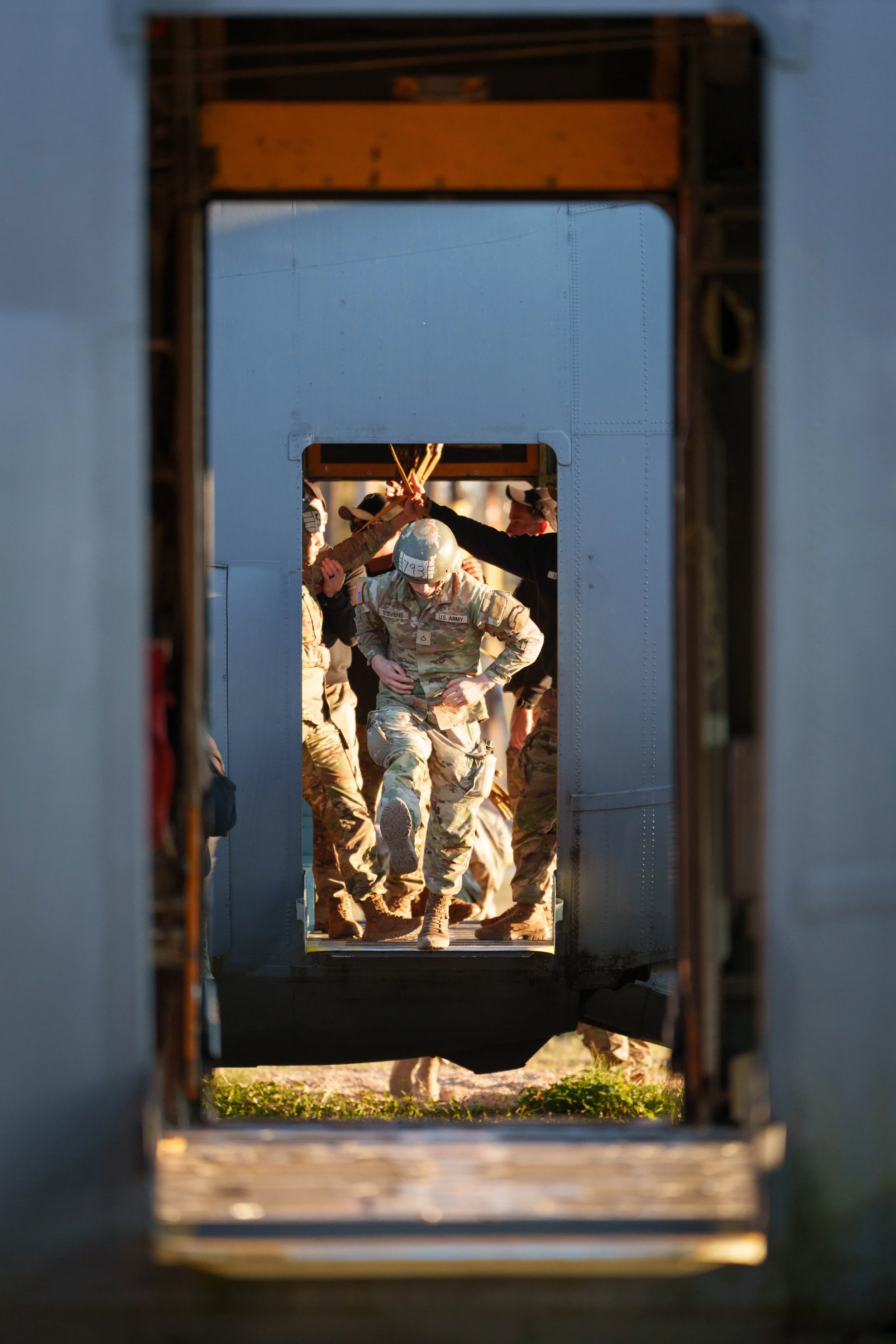Military personnel in uniform climbing down a narrow hatchway on a blue aircraft or military vessel.