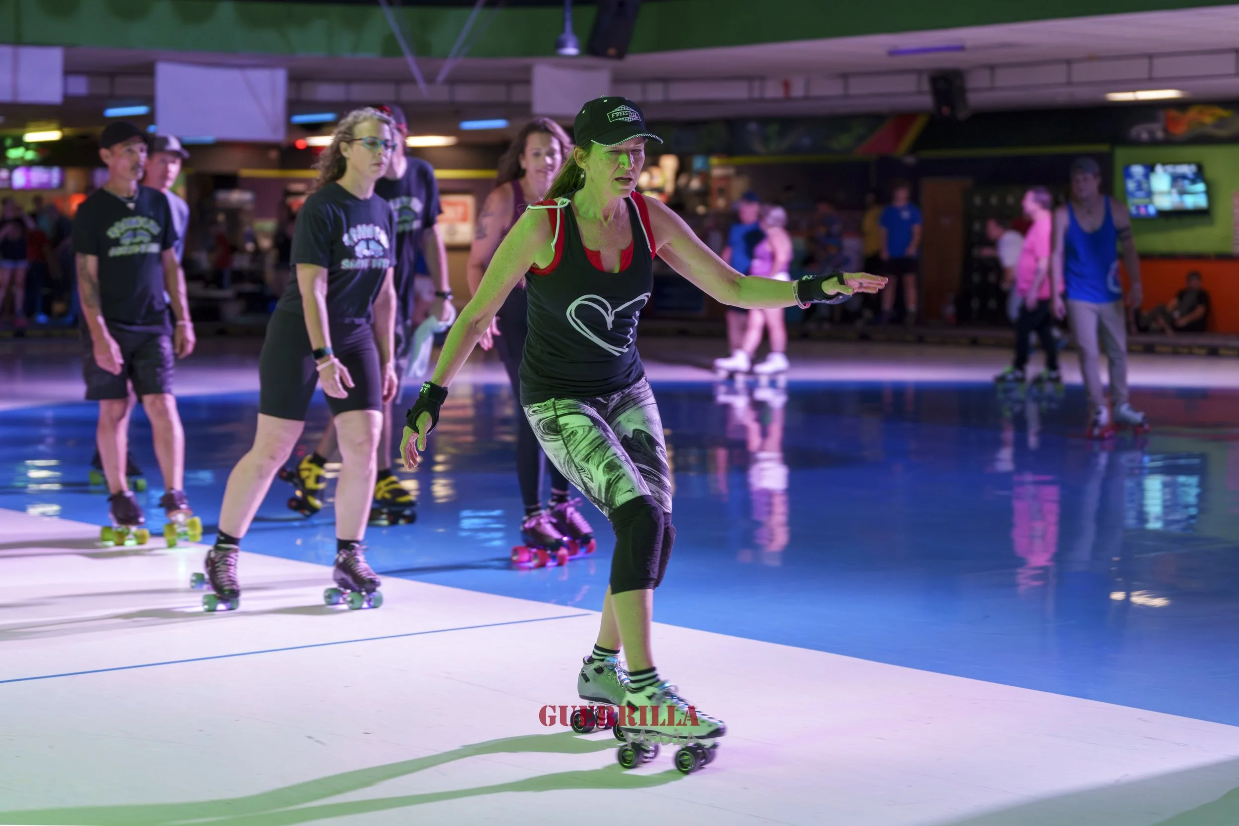 A woman rollerskating on an indoor rink with a group of people in the background.