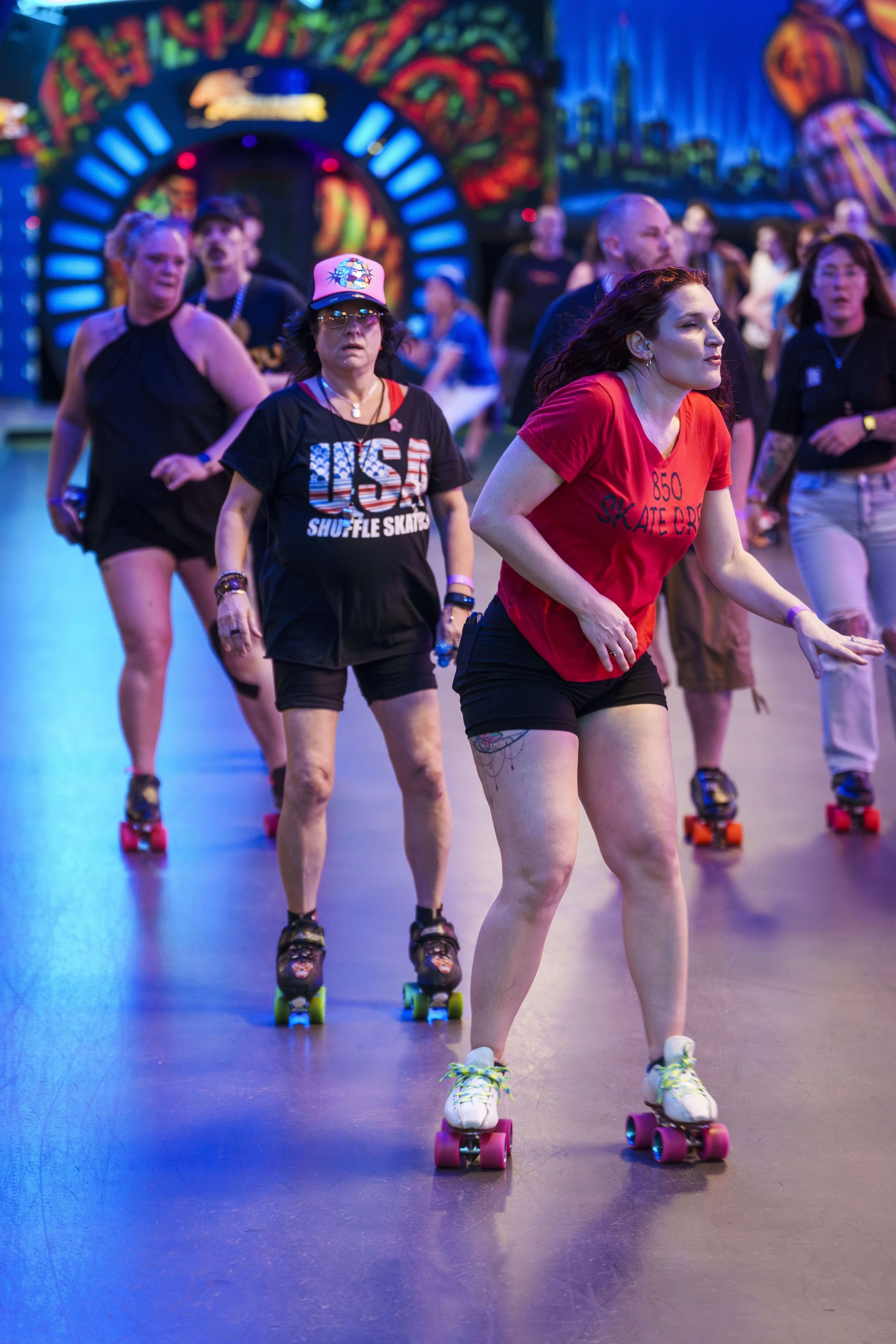 People roller skating inside an amusement park with vibrant, colorful murals and neon lights in the background.