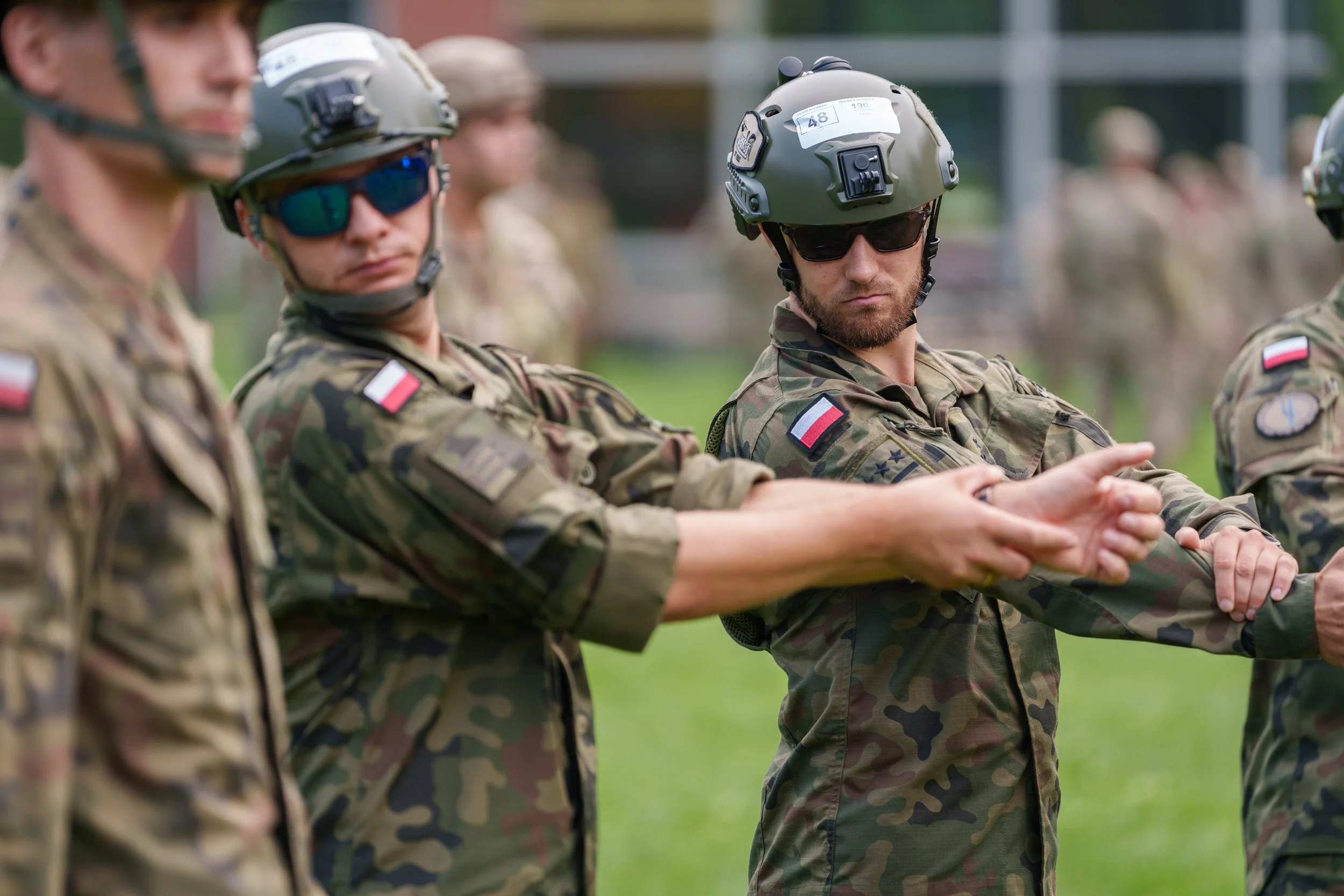 Group of soldiers in camouflage uniforms and helmets, participating in a military training or ceremony outdoors.