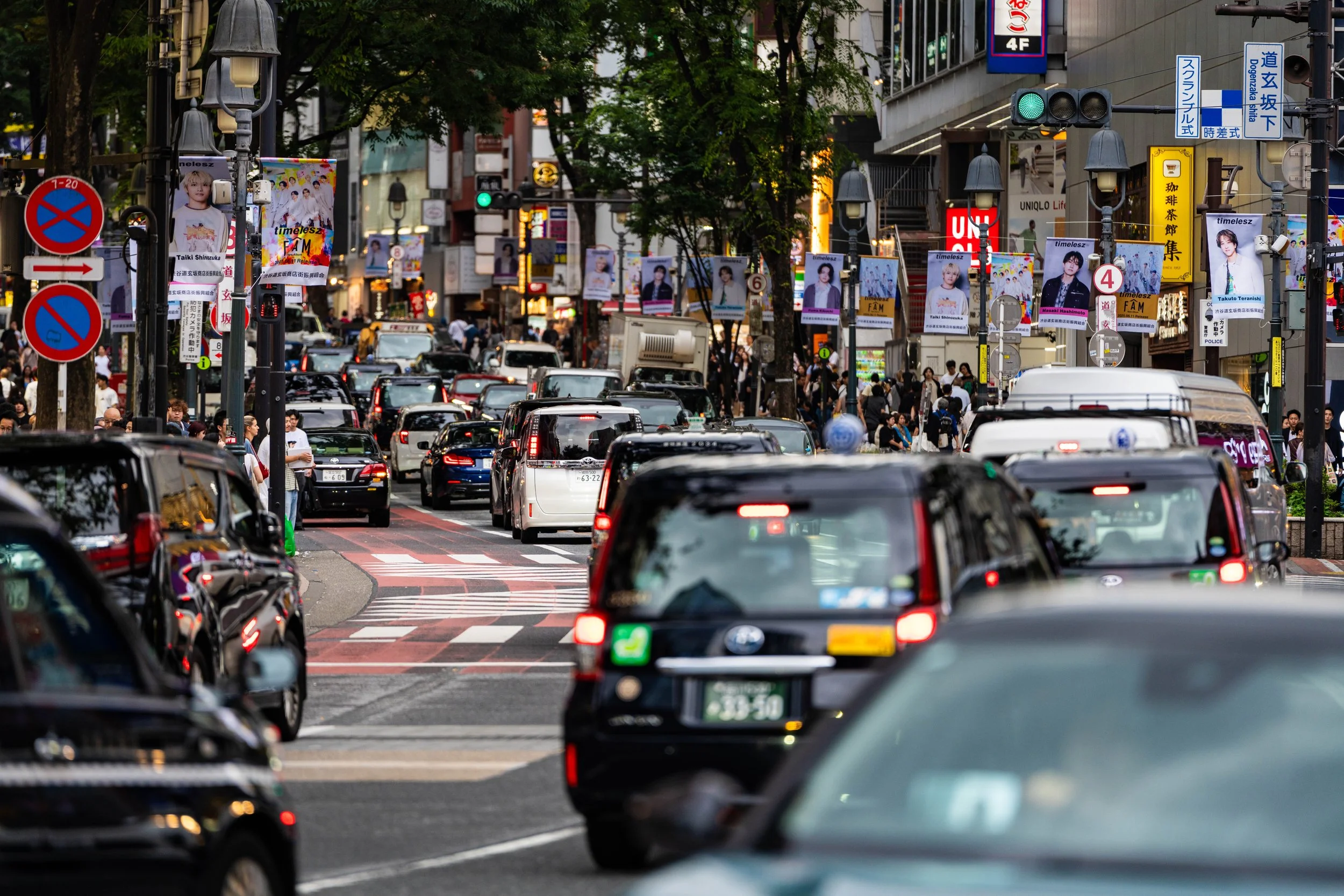 Busy city street filled with cars, pedestrians, and advertising signs in an urban area.