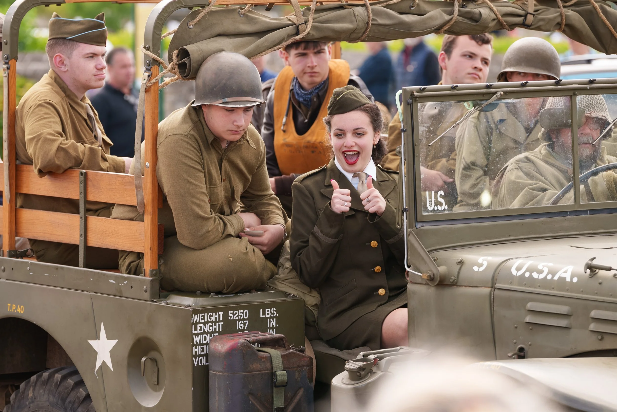 People dressed as WWII soldiers and a woman in a vintage military uniform on an open military vehicle.