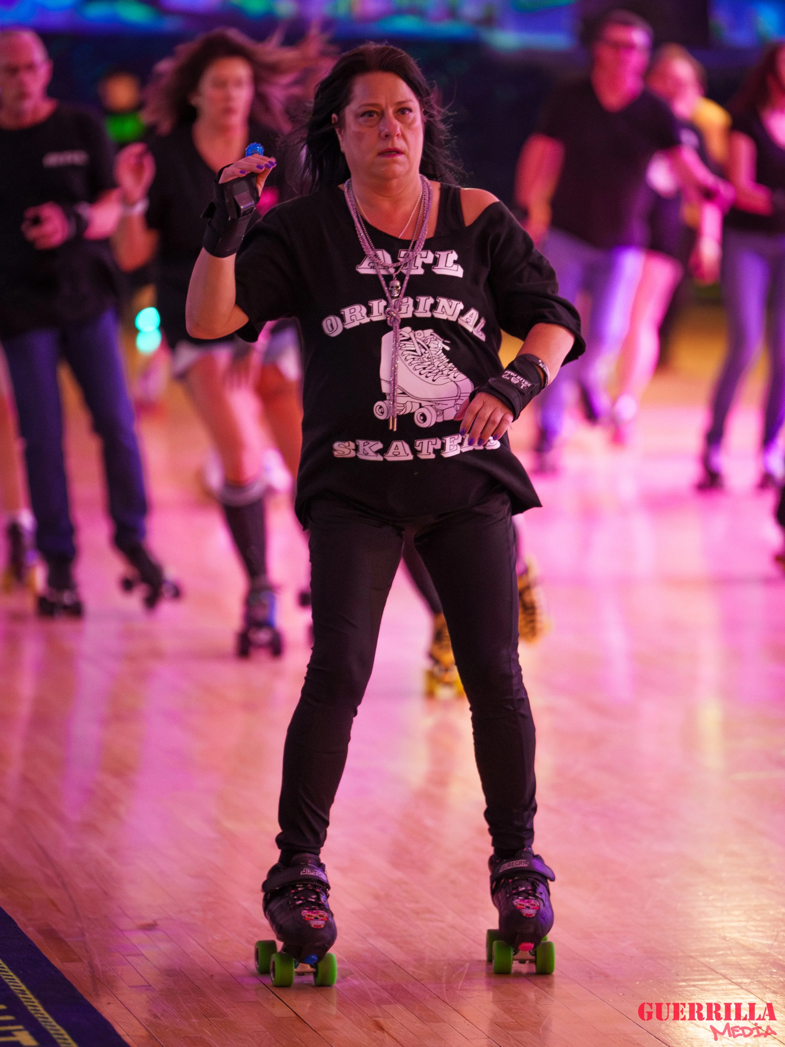 Woman roller skating on a wooden floor with a group of people in the background, under colorful lighting.