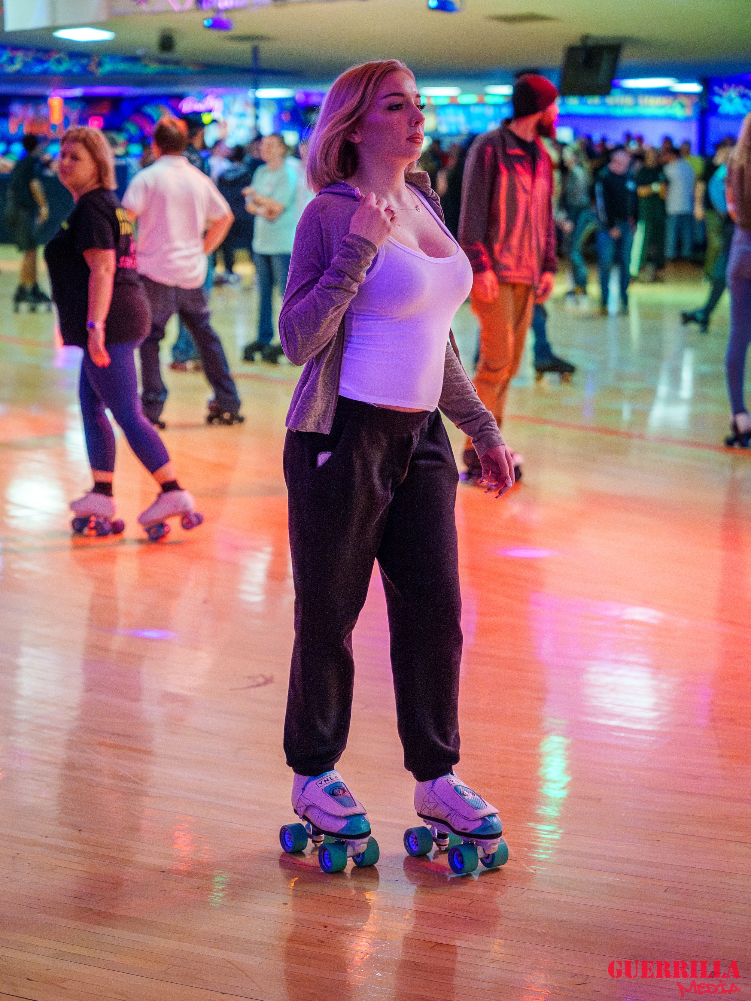 A woman on roller skates at a roller rink, with colorful lights and other skaters in the background.
