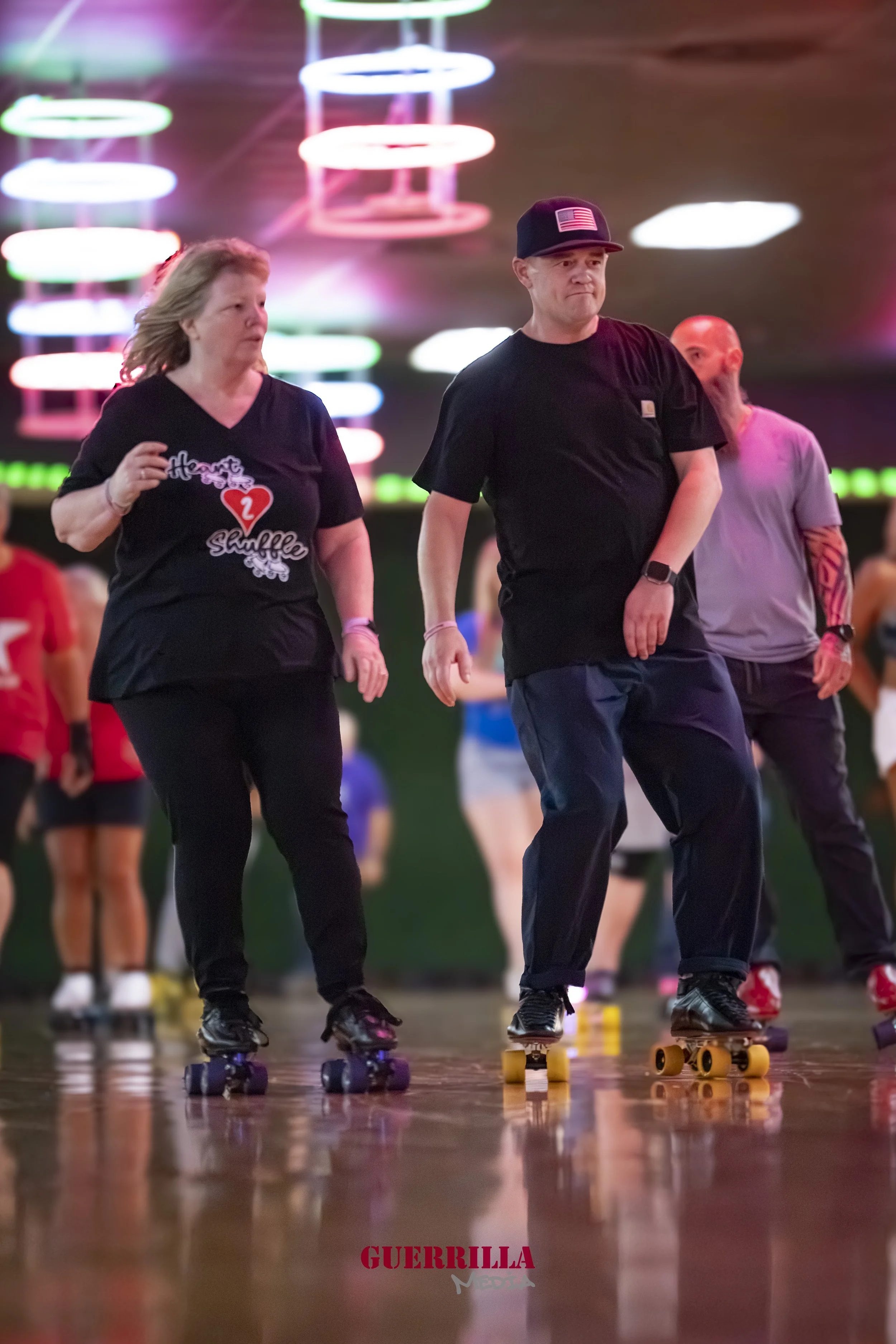 People roller skating indoors at a rink with colorful neon lights in the background.