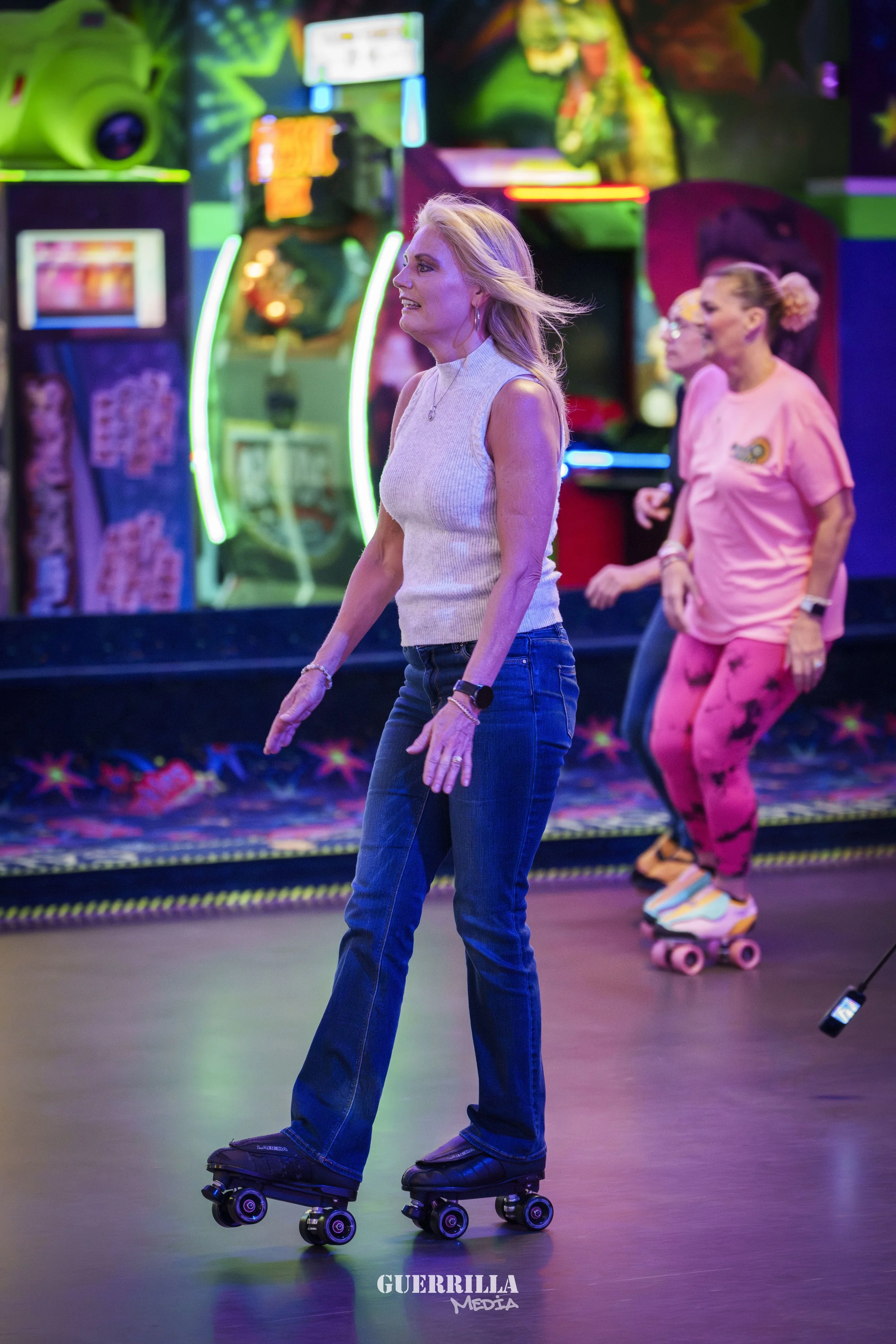 Women roller skating in an arcade with colorful neon lights and arcade games in the background.