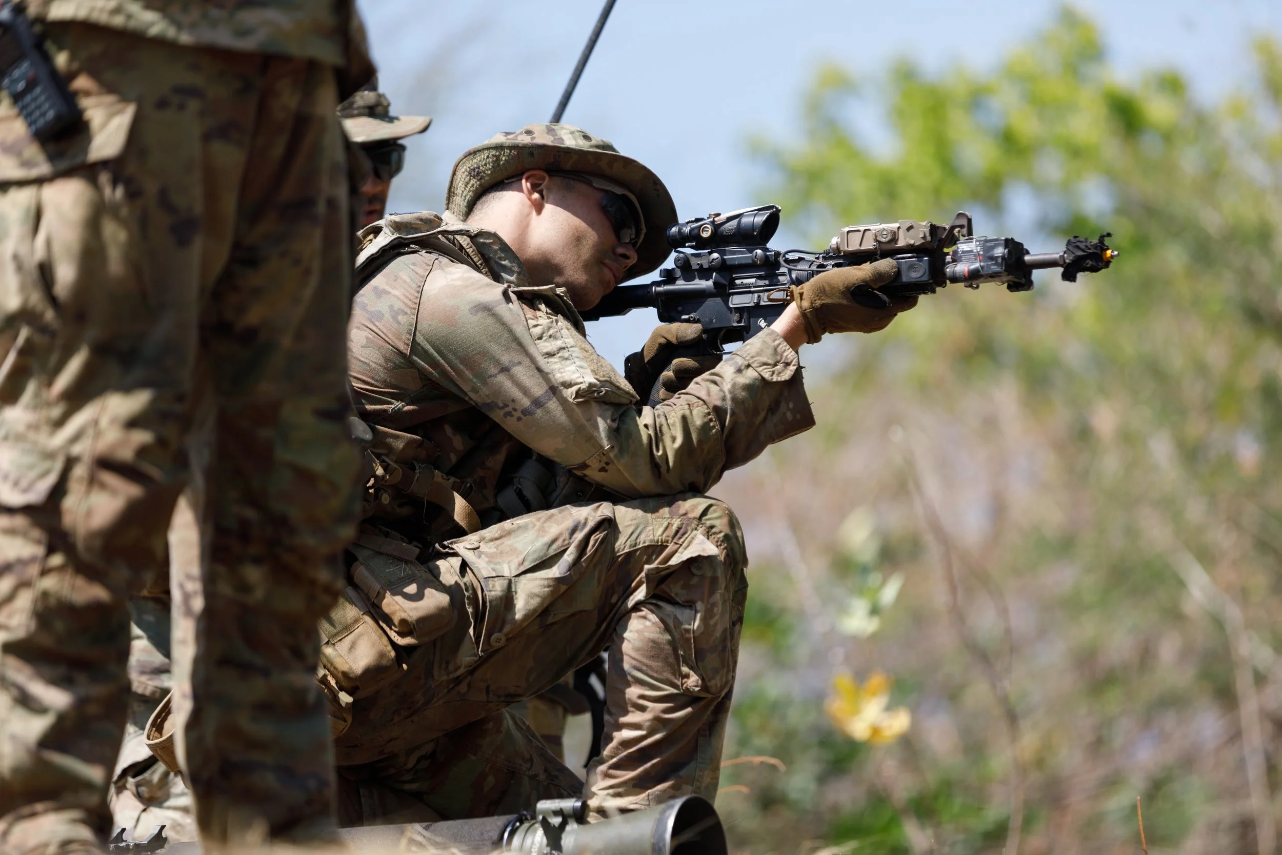 Soldier in camouflage uniform aiming with a sniper rifle during outdoor training.