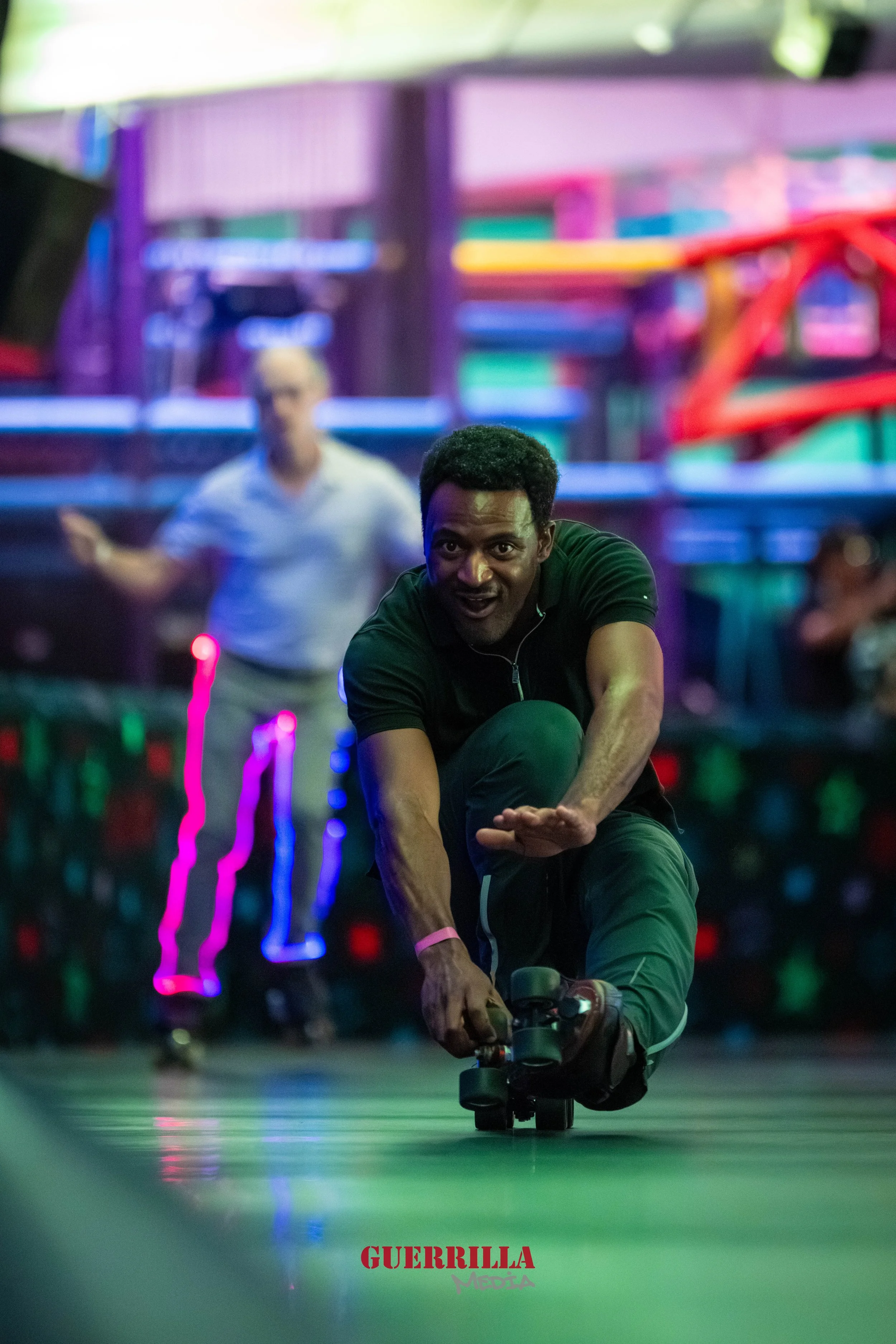 A man roller skating and balancing on one foot in a colorful indoor roller skating rink, with neon lights and other skaters in the background.