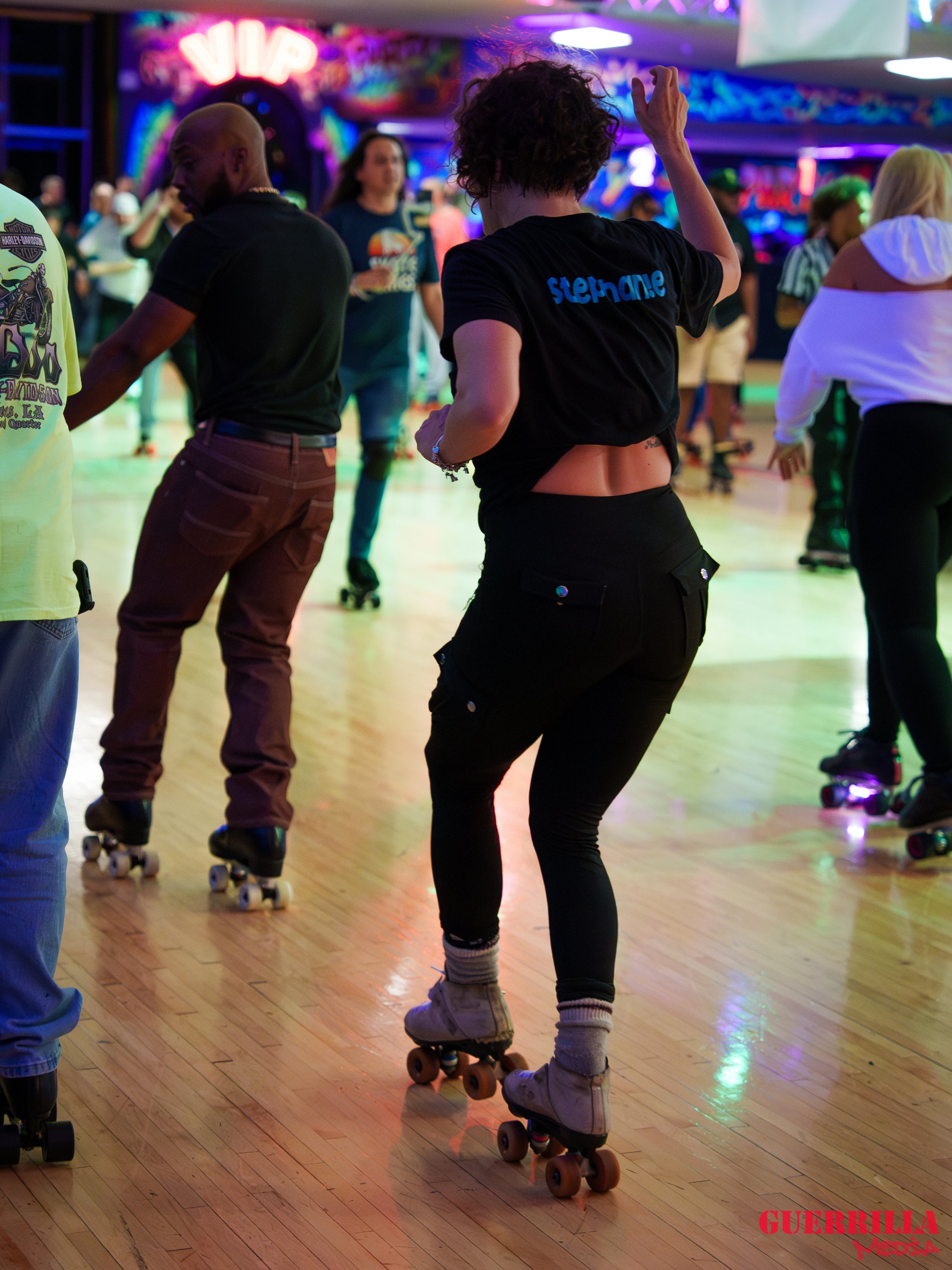 People roller skating in a roller rink with vibrant, colorful lighting and a neon sign in the background.