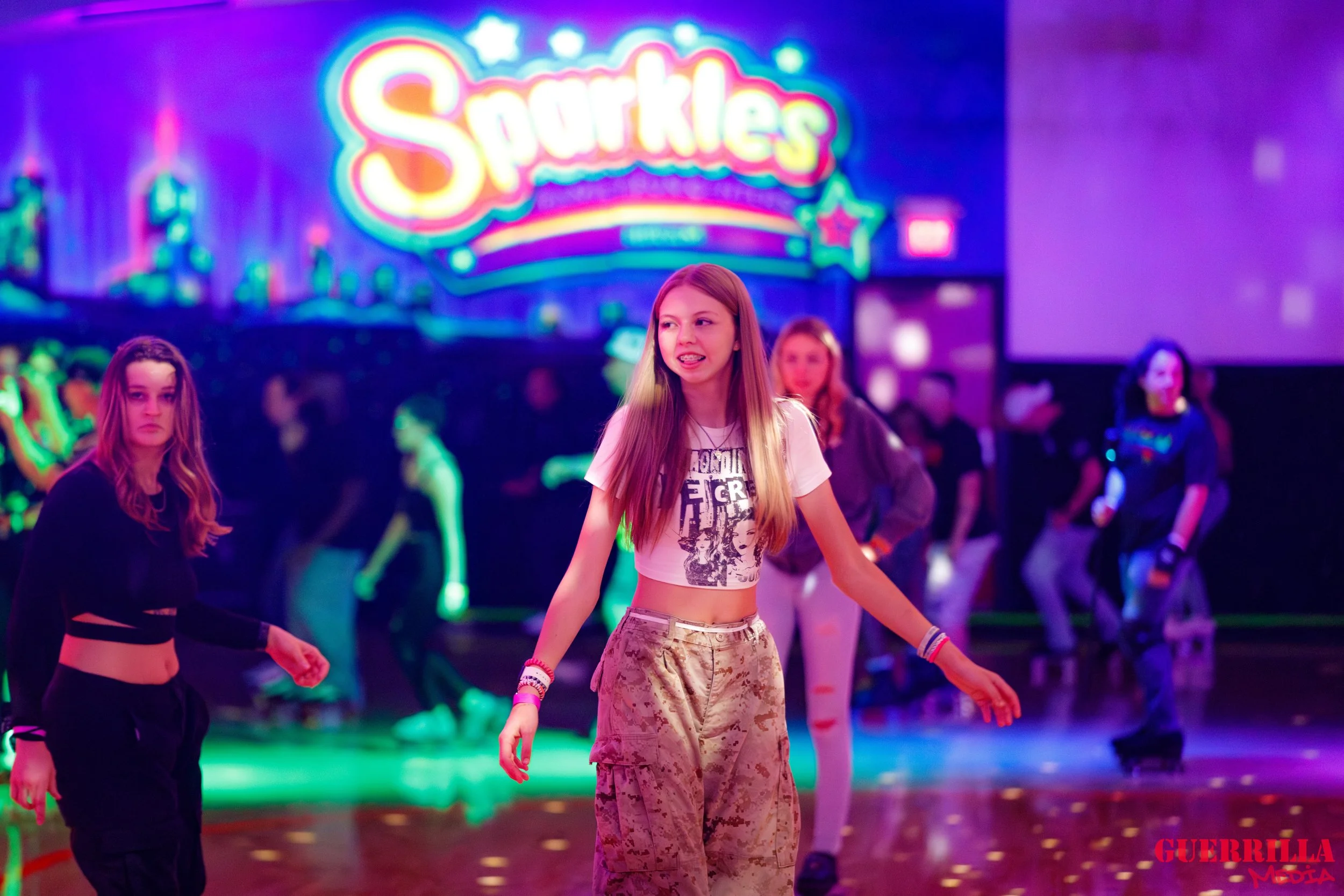 Group of girls roller skating in a neon-lit roller rink with a colorful sign that says Sparkles in the background.