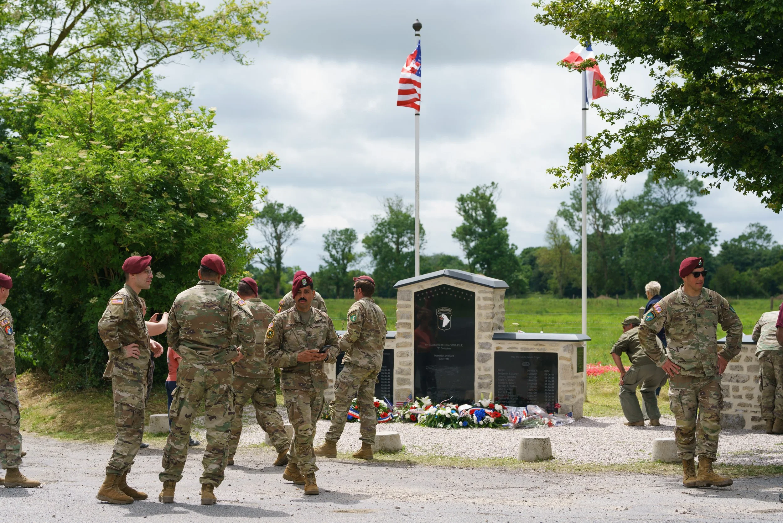 Military personnel gathered at a memorial with flags and flowers during a commemorative event.