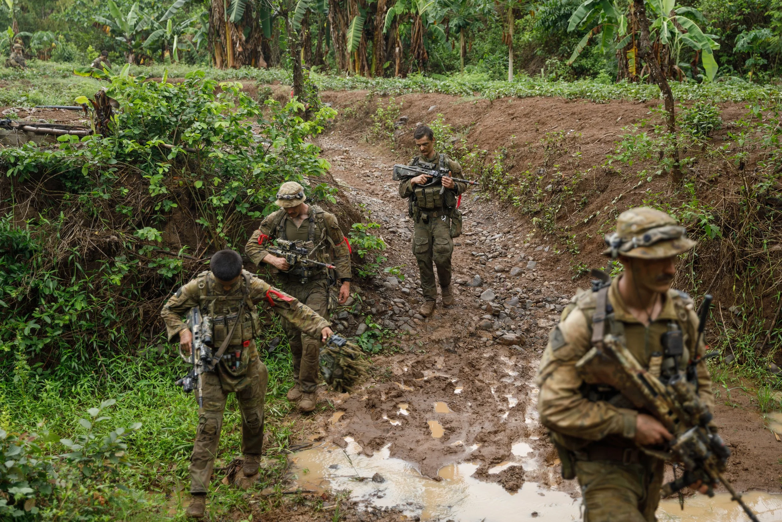 Group of soldiers walking along a muddy path through a lush, green jungle environment.