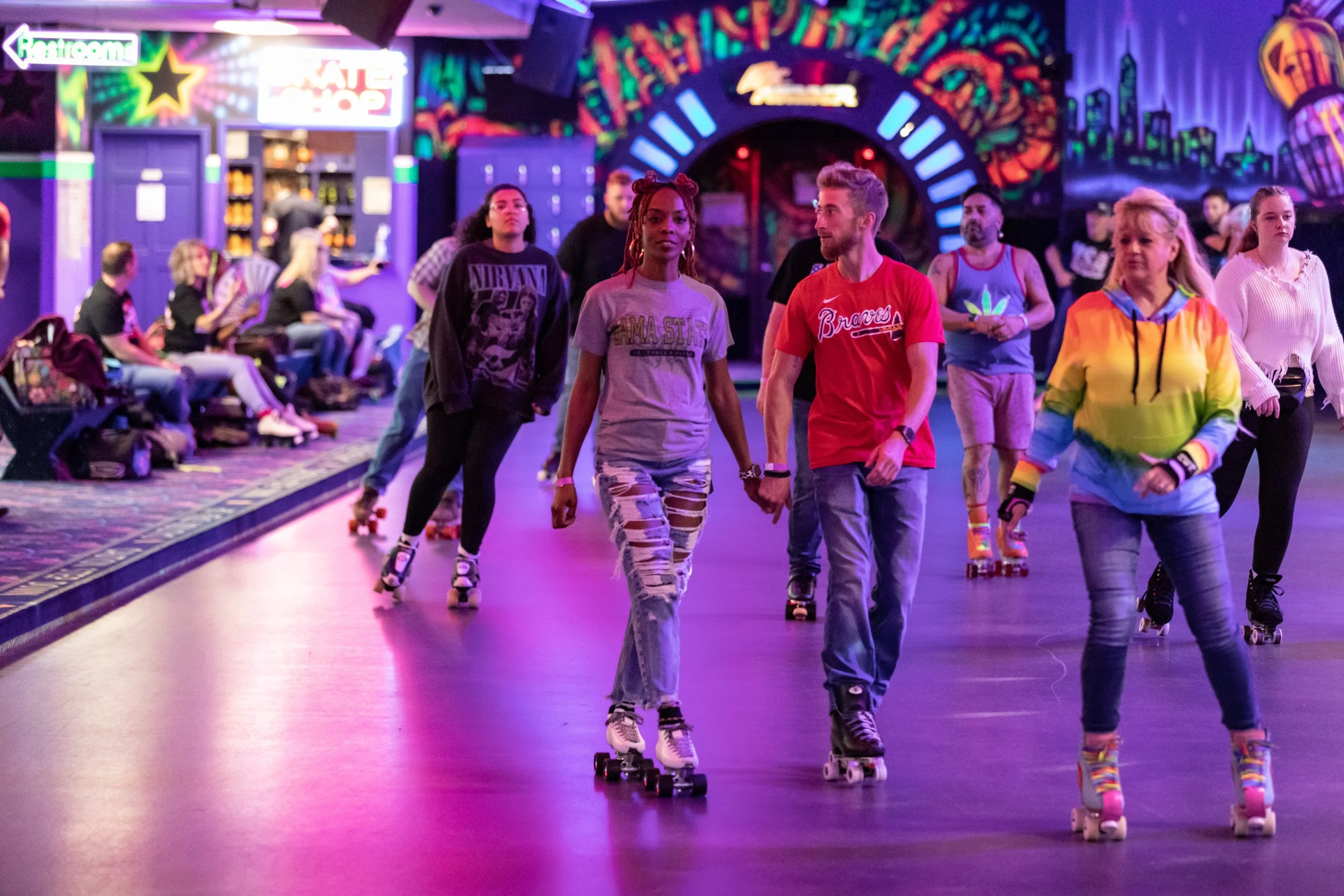 Group of people roller skating inside a roller rink with colorful neon lights and graffiti-style artwork on the walls.