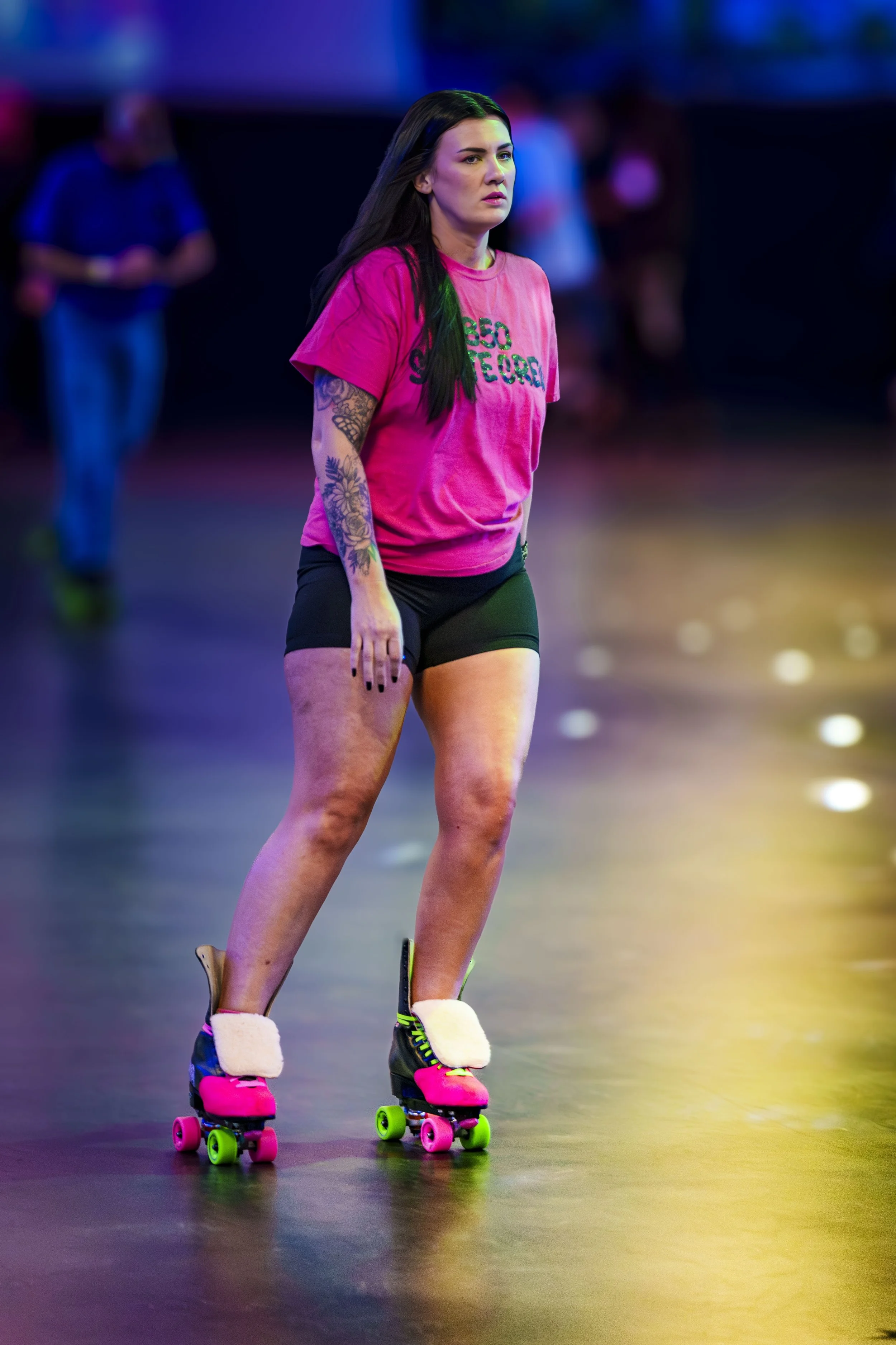 A woman in pink shirt and black shorts on roller skates in an indoor skating rink.