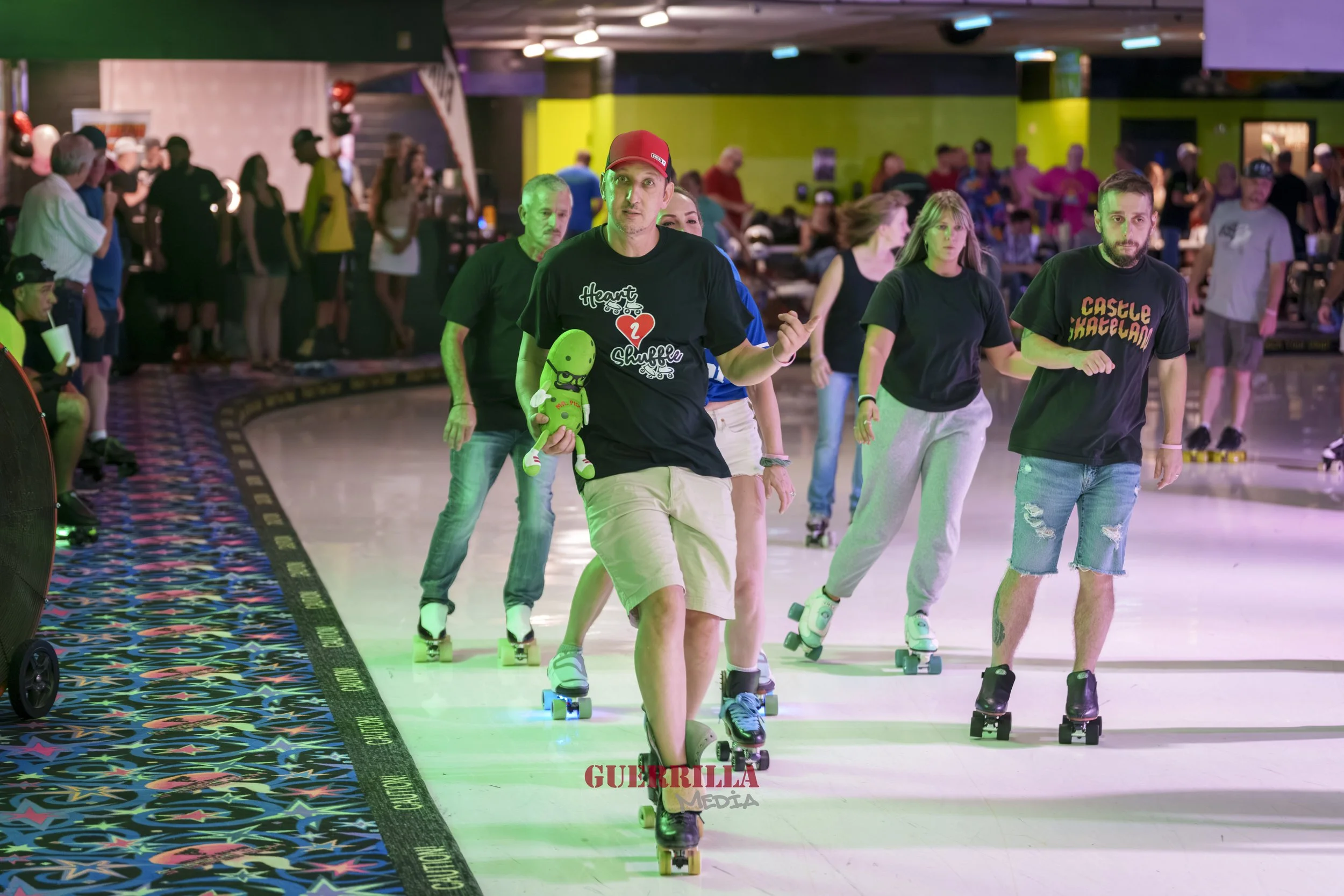 People roller skating inside an entertainment rink with colorful lighting and a patterned carpet edge.