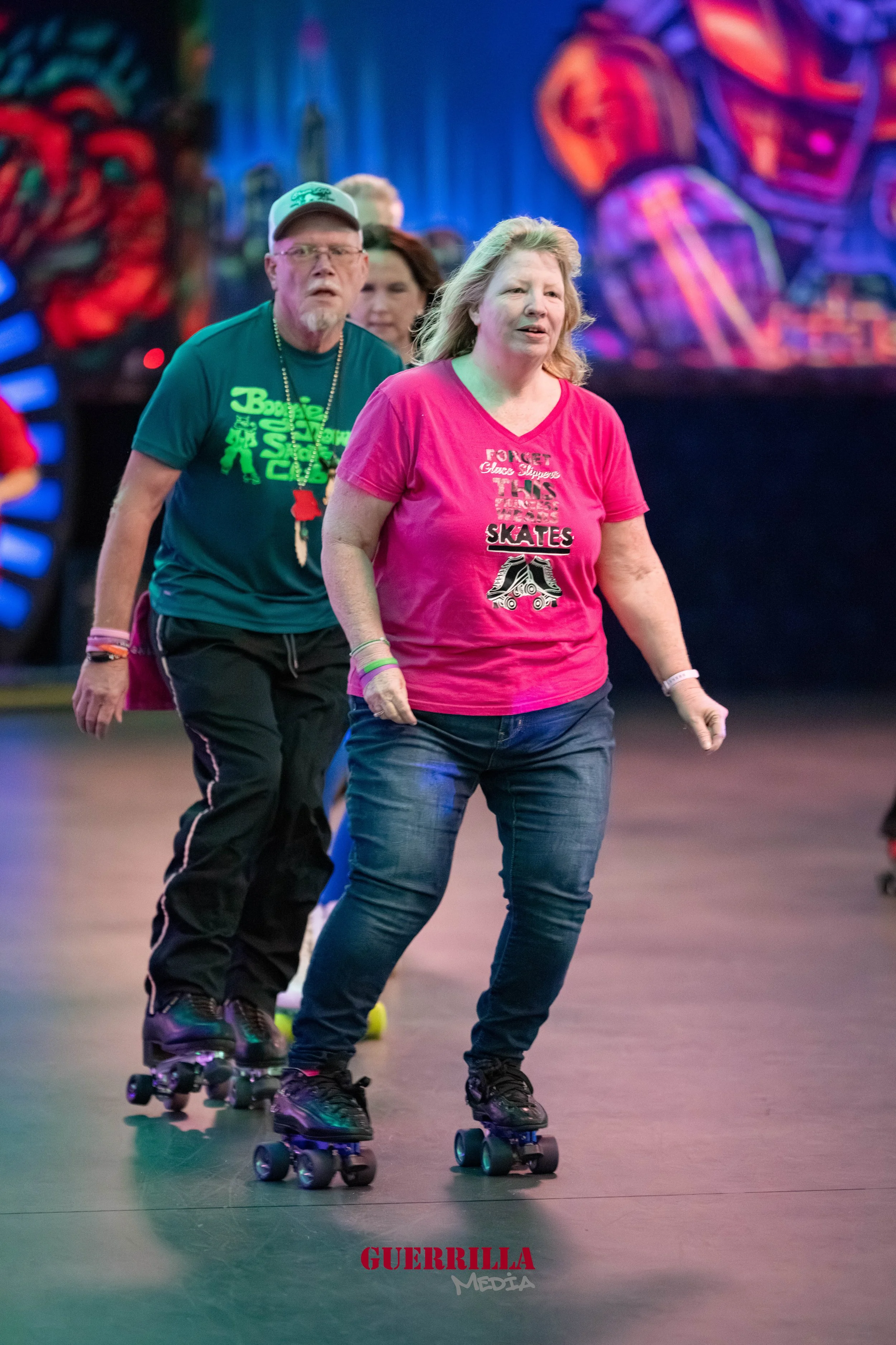 People roller skating indoors with colorful graffiti art in the background, including a man in a green shirt and a woman in a pink shirt leading the group.