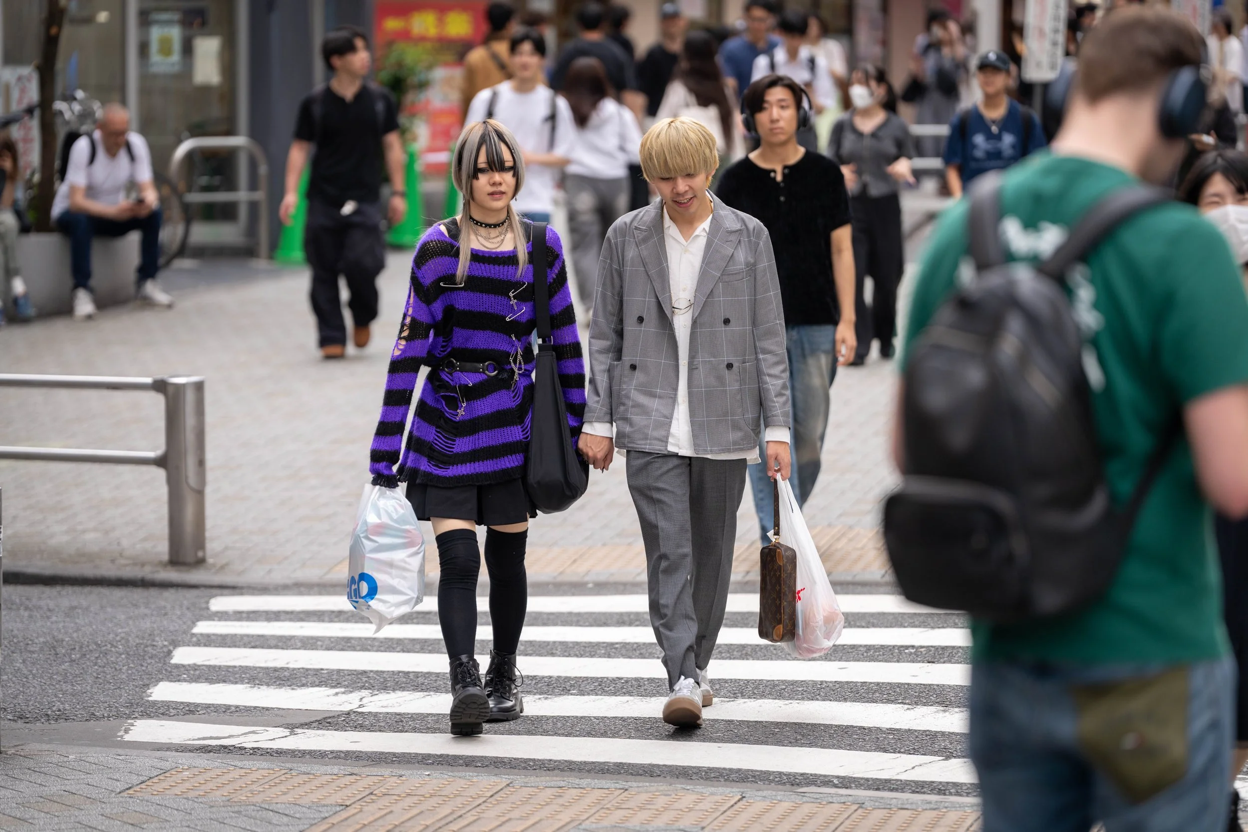 Two young people holding hands crossing a busy street with pedestrians in the background.
