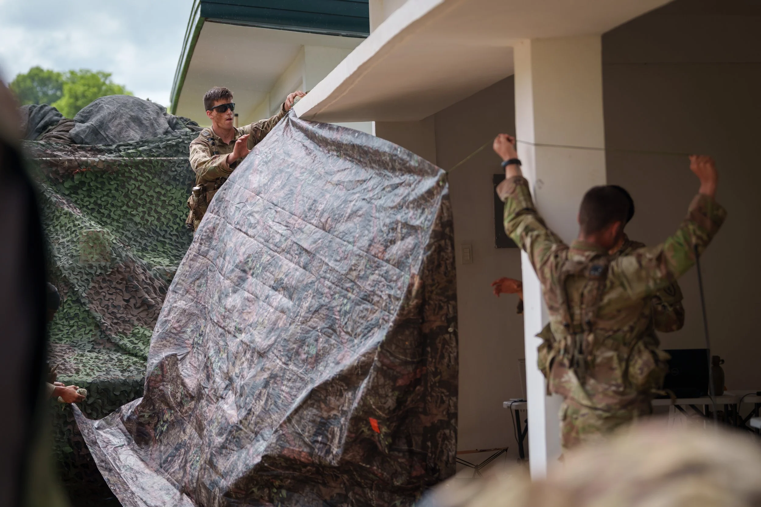 Military personnel setting up camouflage netting inside a building.
