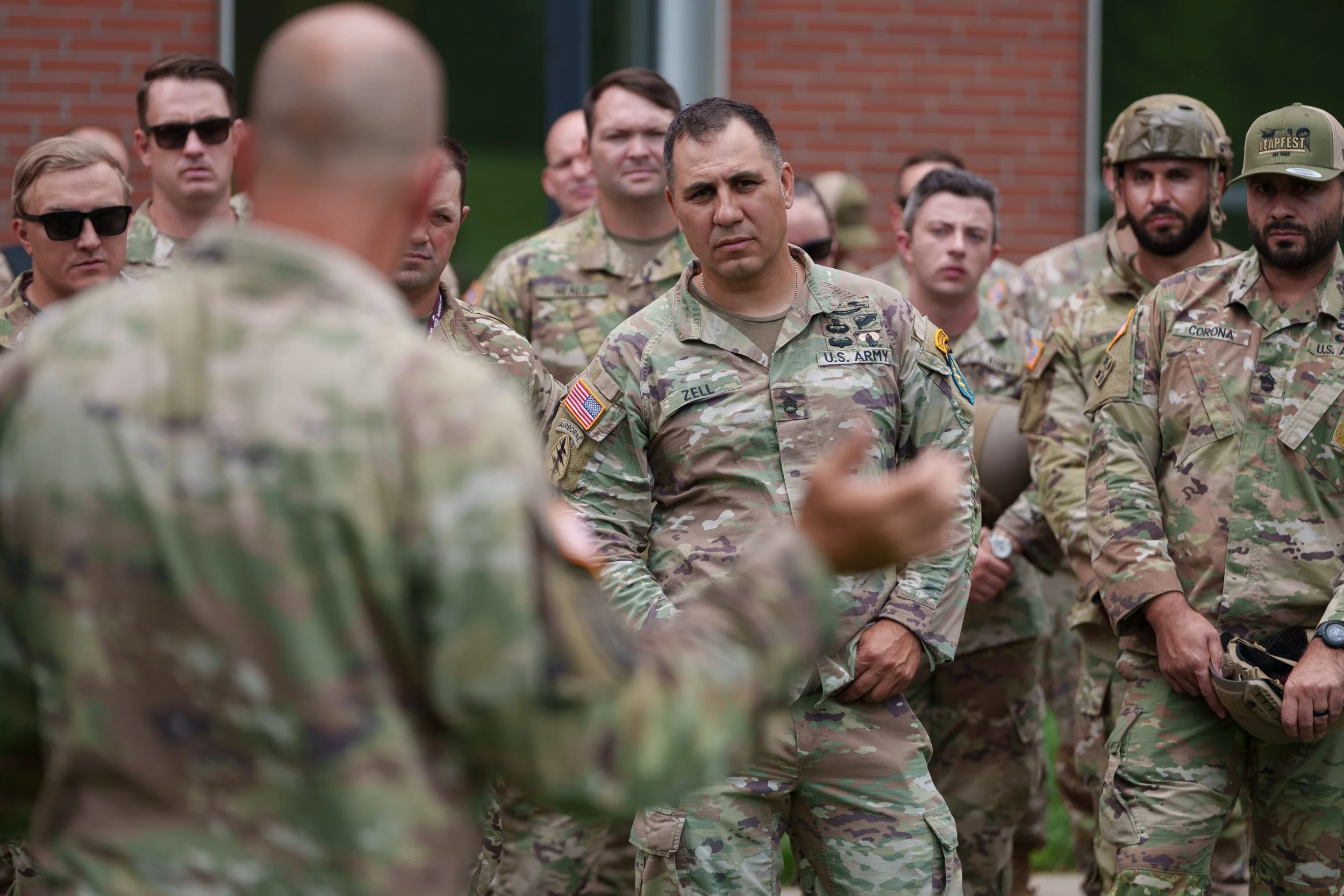 Group of U.S. soldiers in uniform gathered outdoors for a discussion, with one soldier speaking while others listen attentively.