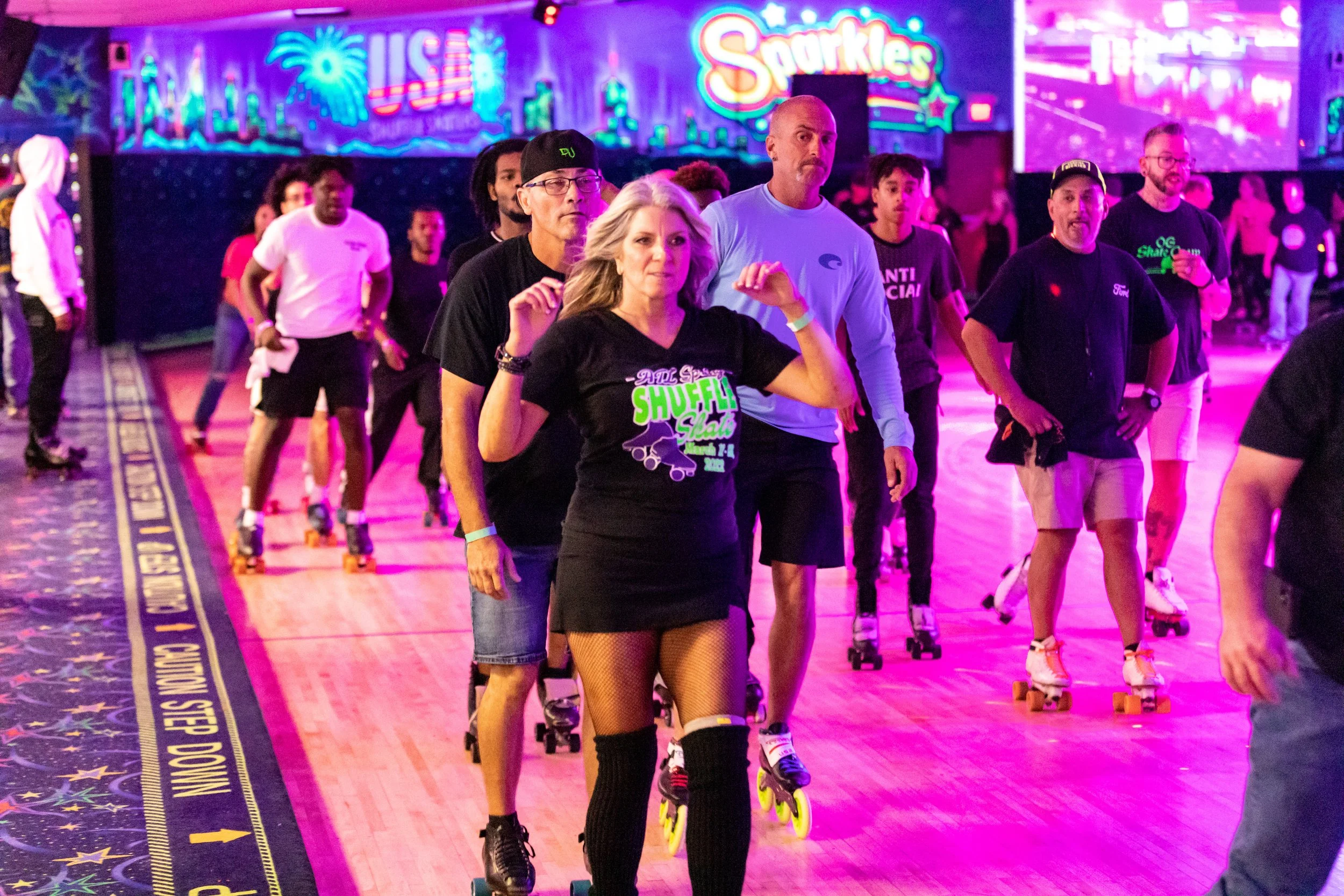 People roller skating at an indoor roller rink with colorful neon signs and lights in the background.