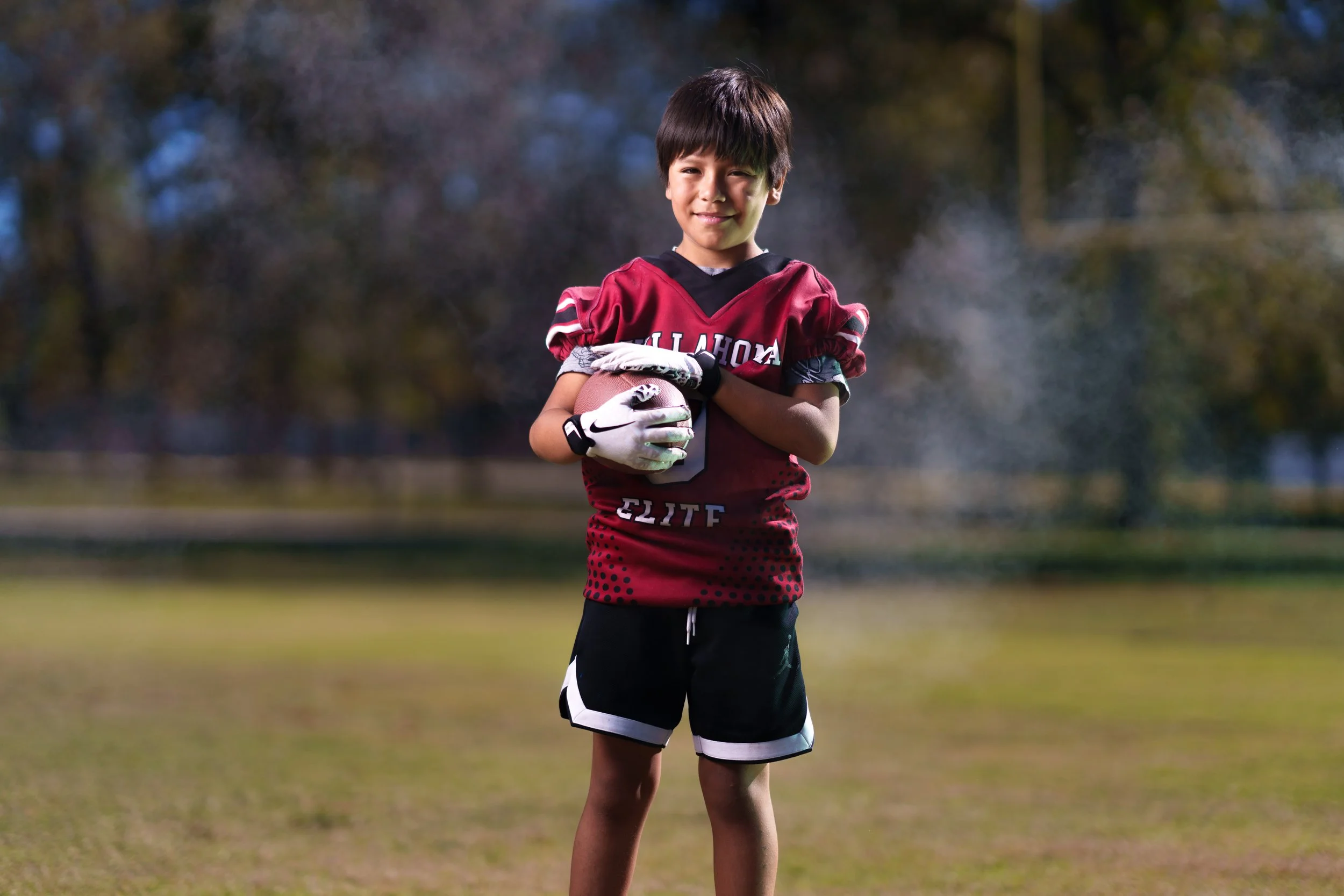 A young boy in a football uniform holding a football on a football field.
