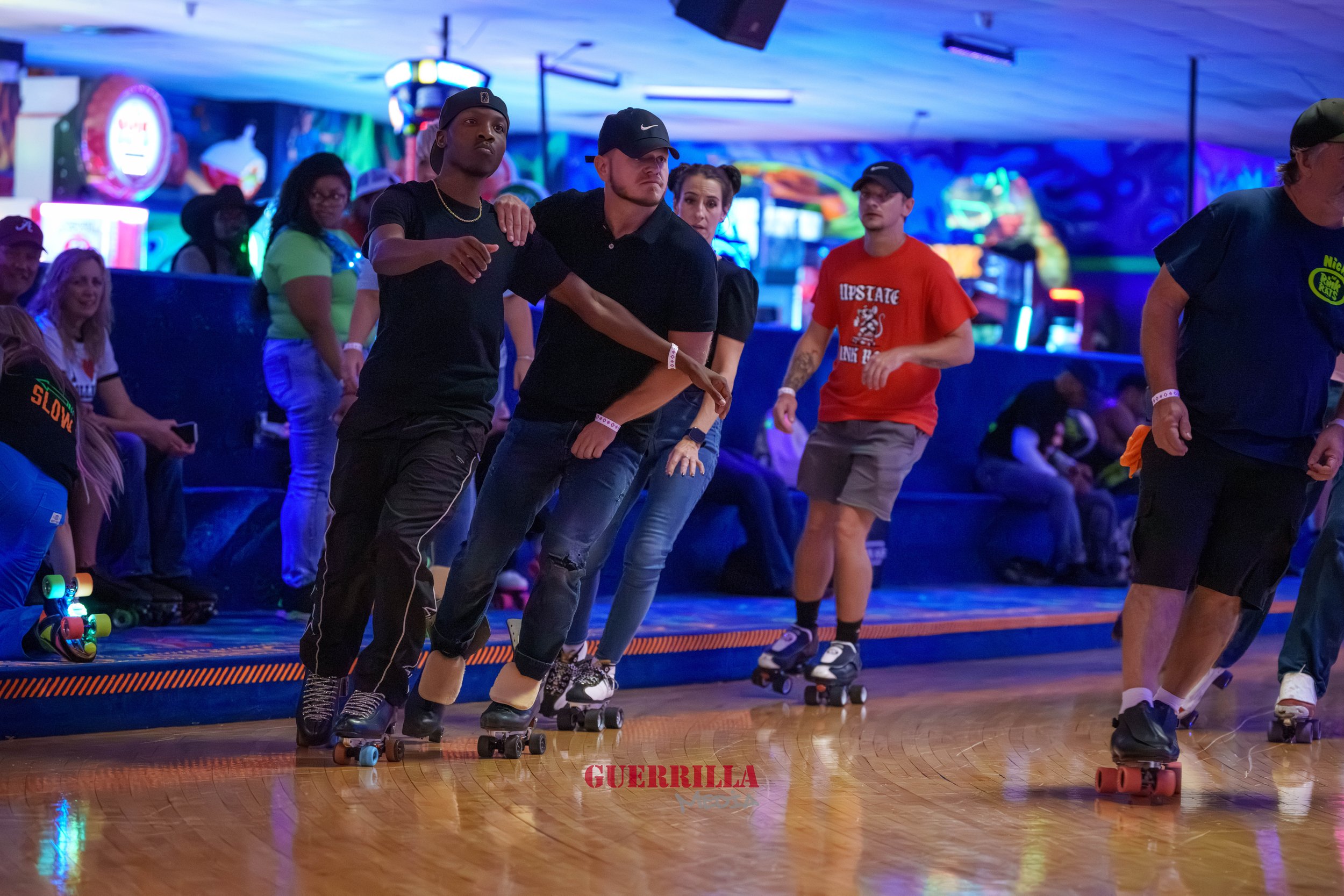 People roller skating at an indoor rink with neon colorful lights and murals in the background.