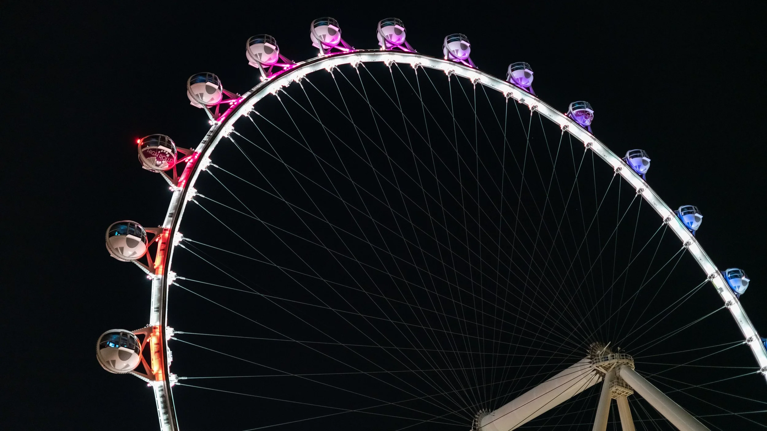 Night view of a brightly lit Ferris wheel with colorful cabins against a dark sky.