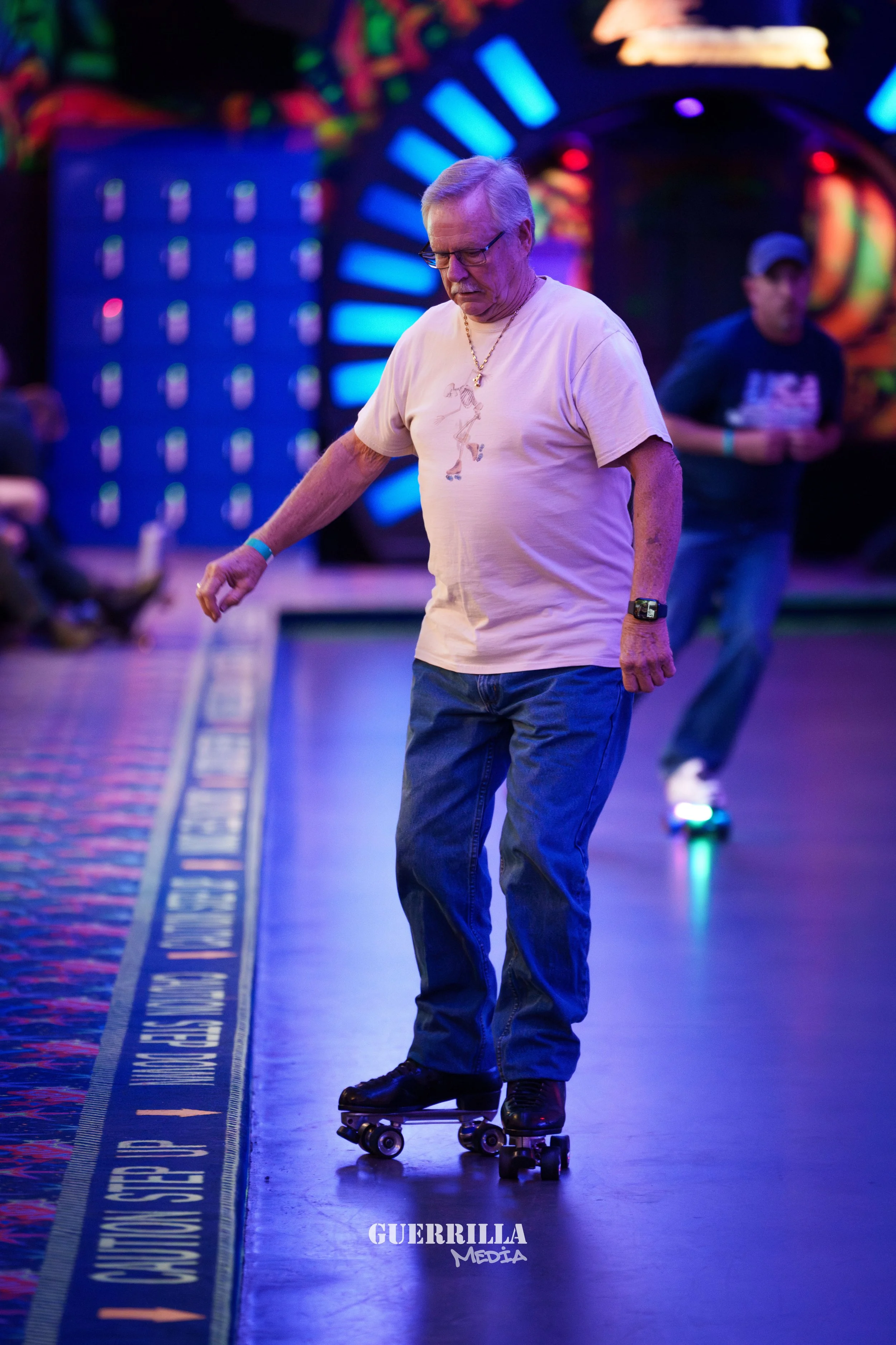 An elderly man with glasses and light-colored hair rollerskating indoors on a roller rink, wearing a beige t-shirt, blue jeans, and a gold chain, with a colorful, vibrant background.