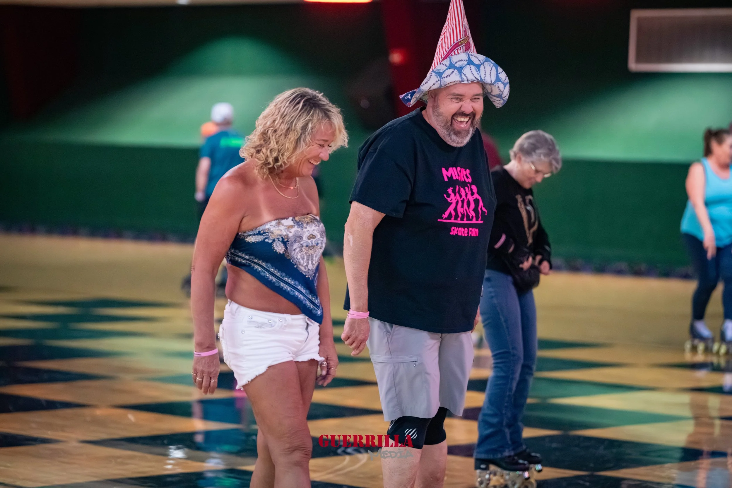 People roller skating inside an indoor skating rink, with green and black walls, and a wooden floor with a black and yellow checkered pattern.