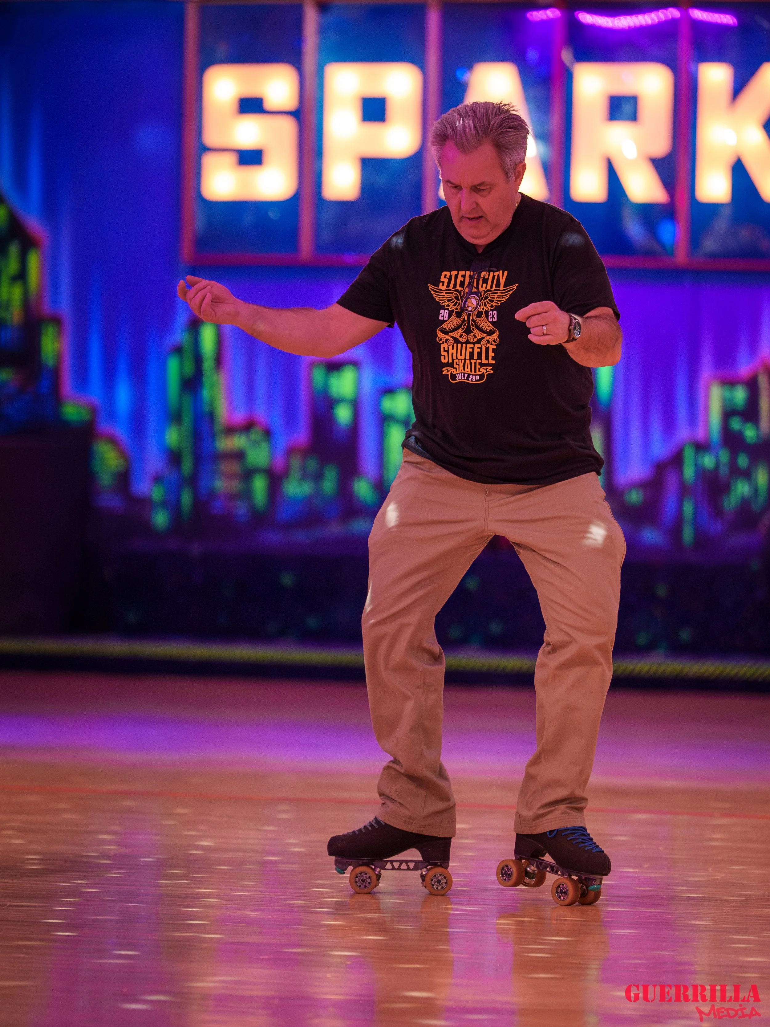 A man roller skating at an indoor roller rink with colorful neon lights and a sign that reads 'SPARK' in the background.