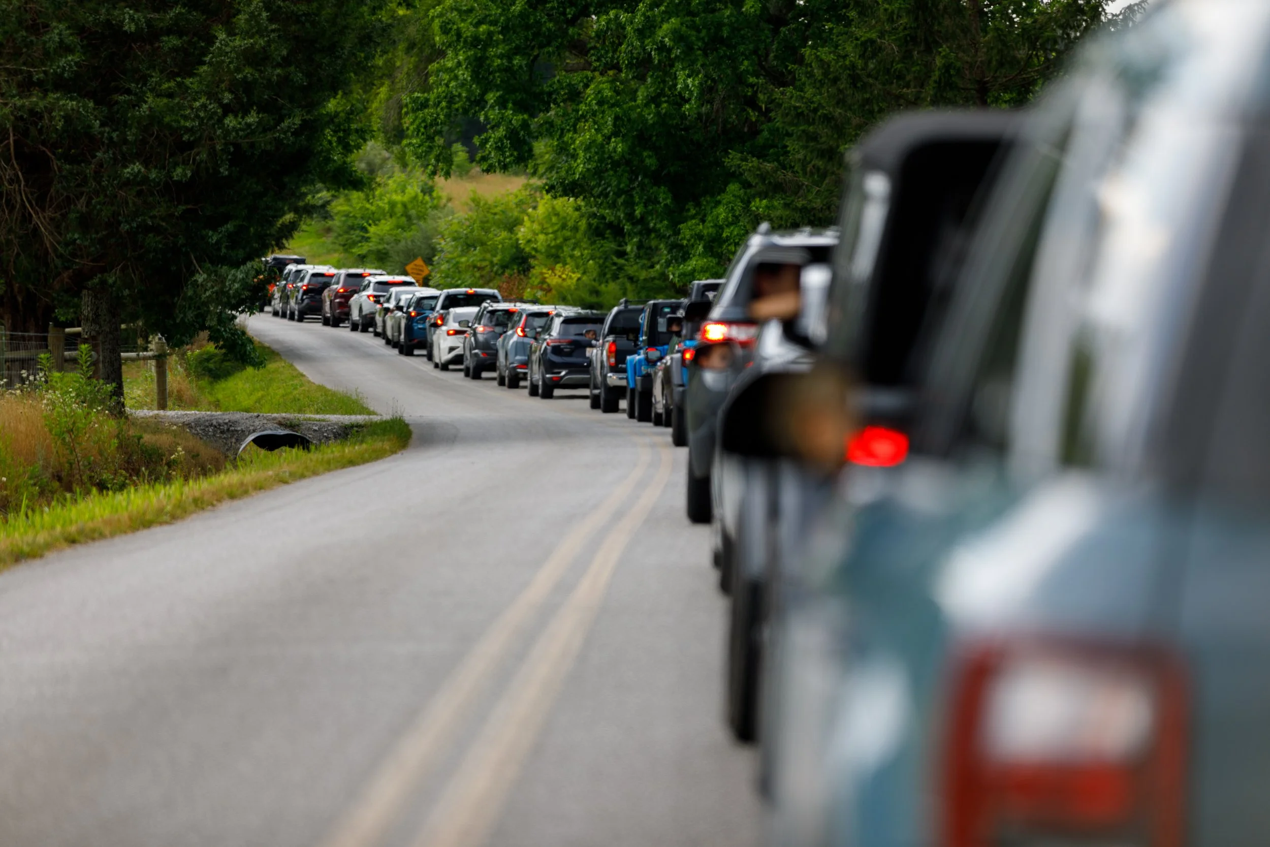 A long line of cars on a rural road with trees on both sides, traffic congestion in the countryside.