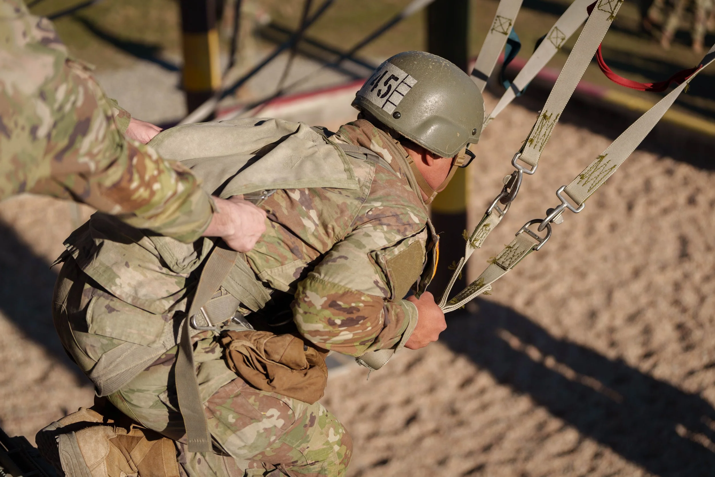 Military personnel in camouflage uniform and helmet participating in a training exercise, climbing a wall using a harness and ropes.