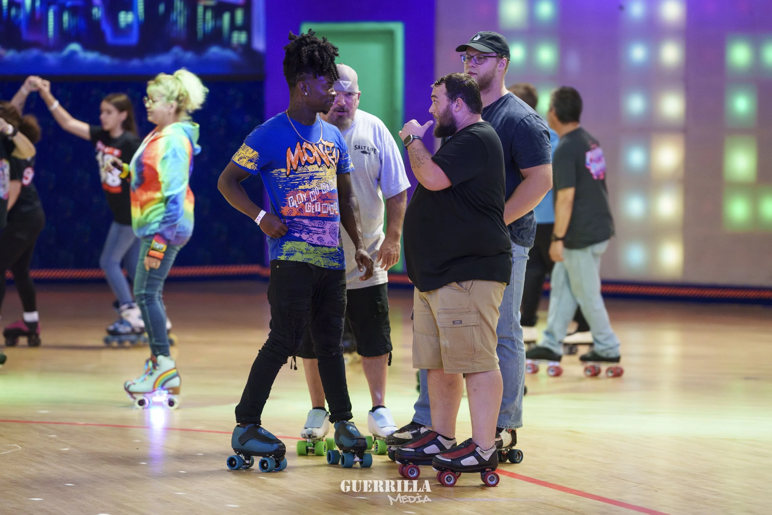 A group of people roller skating indoors, some are skateboarding, with colorful lighting and a vibrant background.